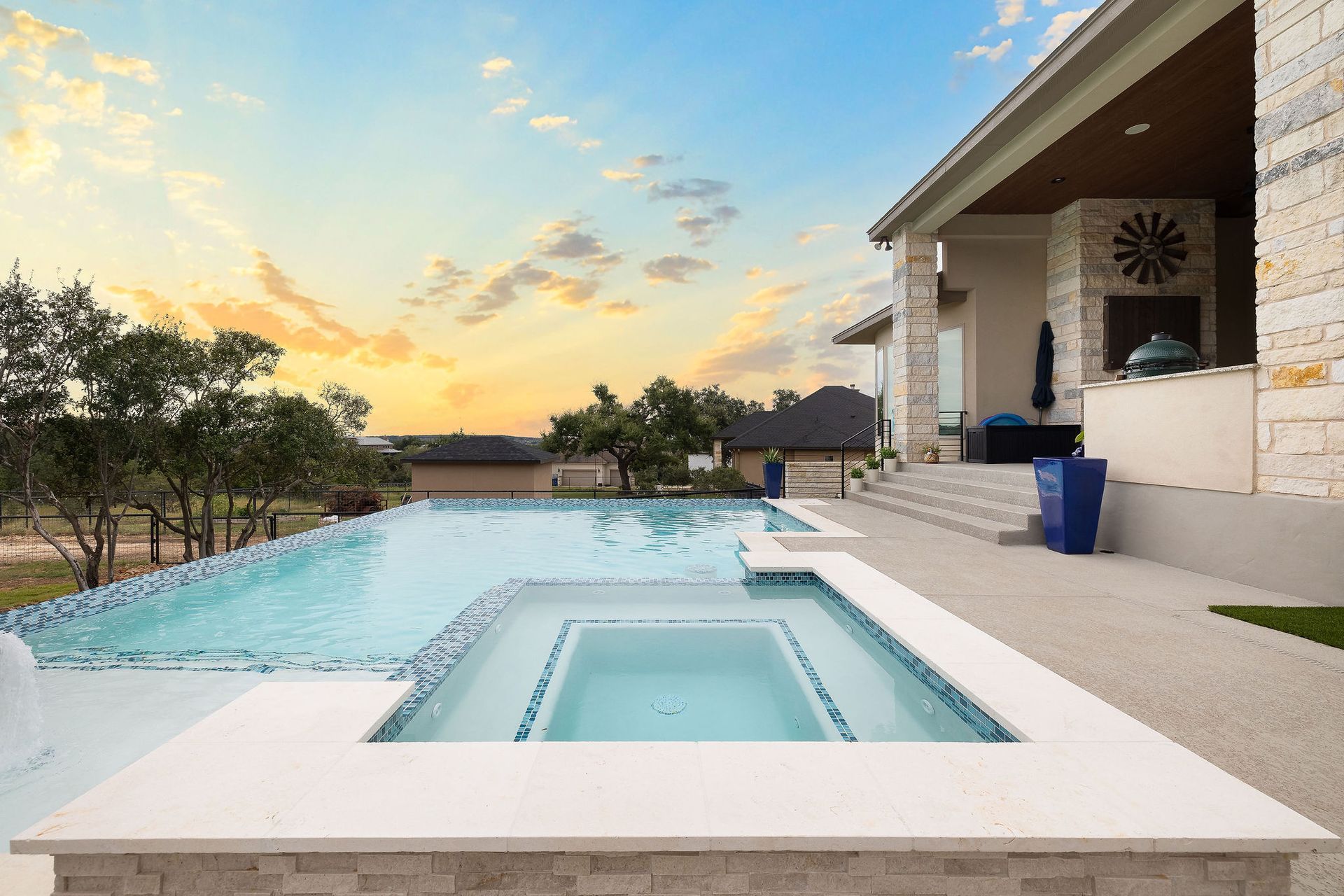 Backyard pool at sunset with a raised hot tub and covered patio beside the water