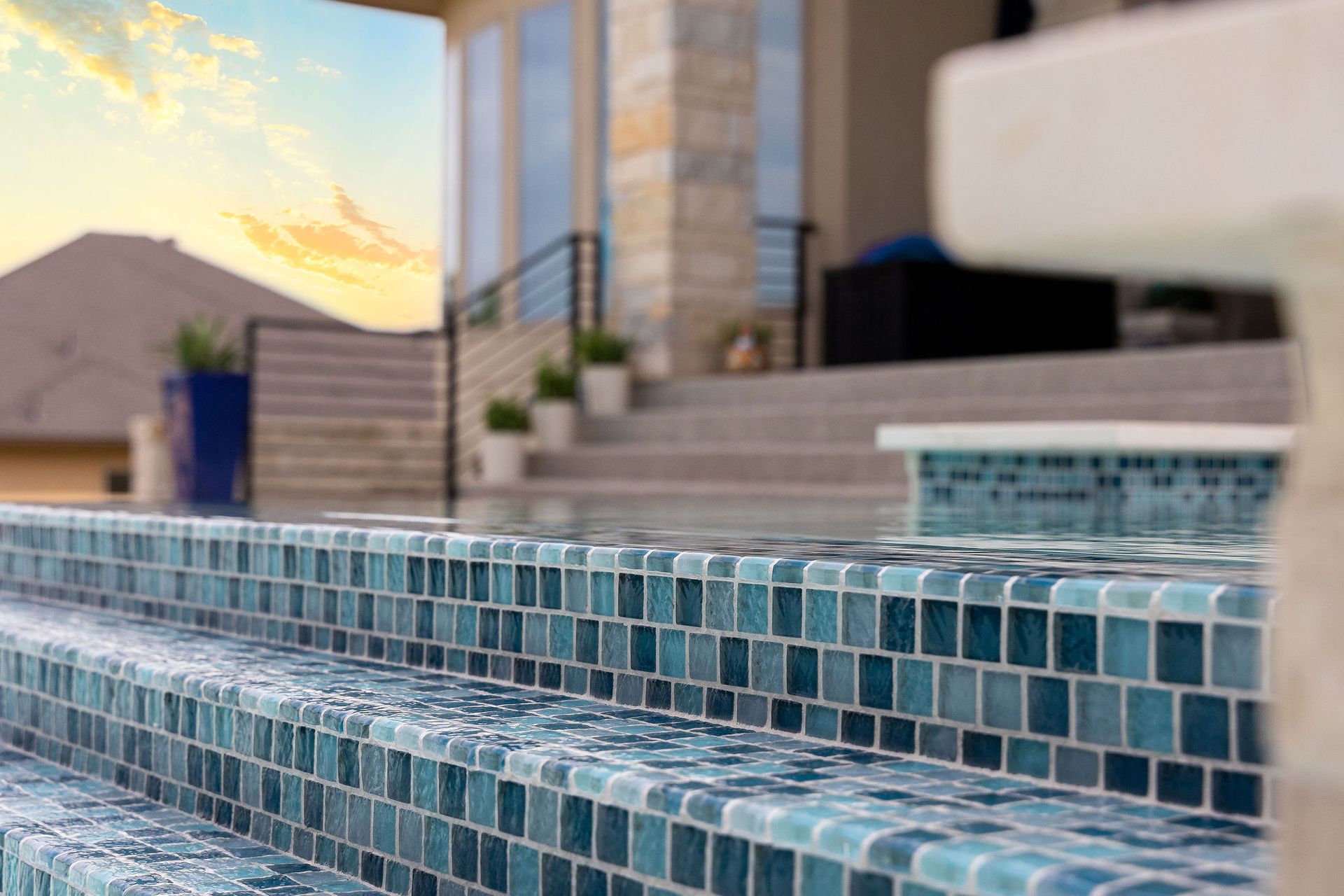 Blue mosaic-tiled pool steps beside a modern house at sunset