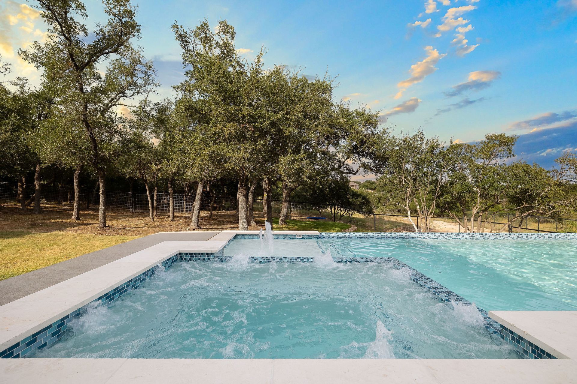 Blue pool and spa in a wooded landscape under a partly cloudy sky