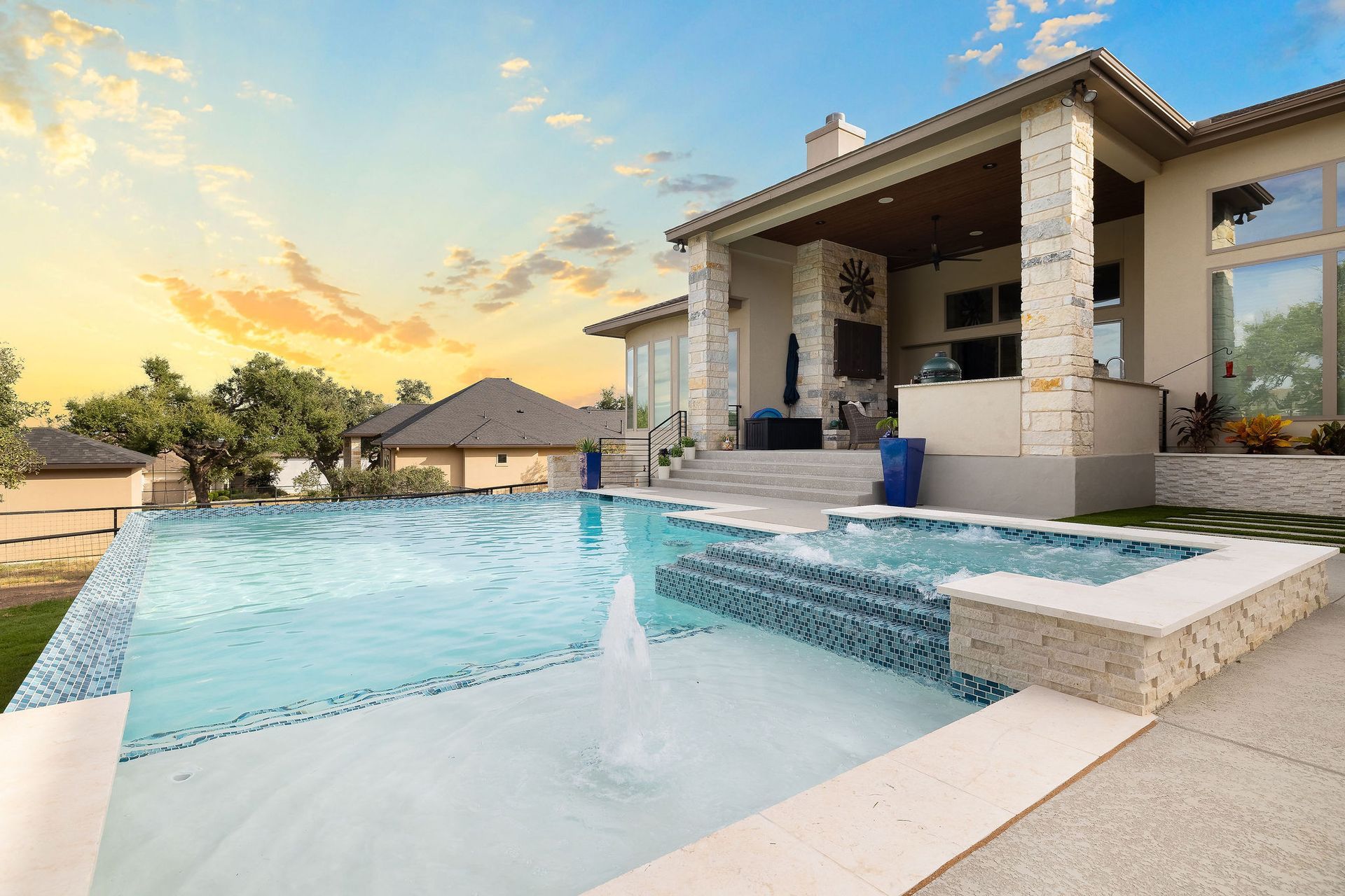 Modern backyard patio with a blue swimming pool, hot tub, and a house at sunset