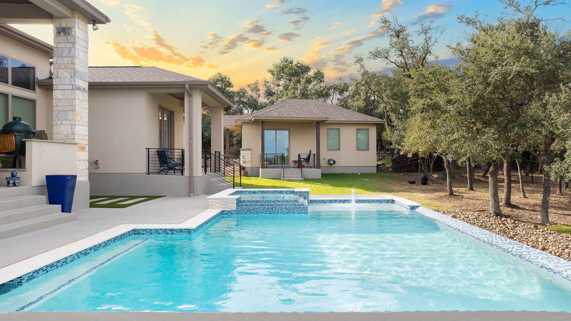 Backyard patio with a swimming pool, modern house, lounge chairs, and trees at sunset