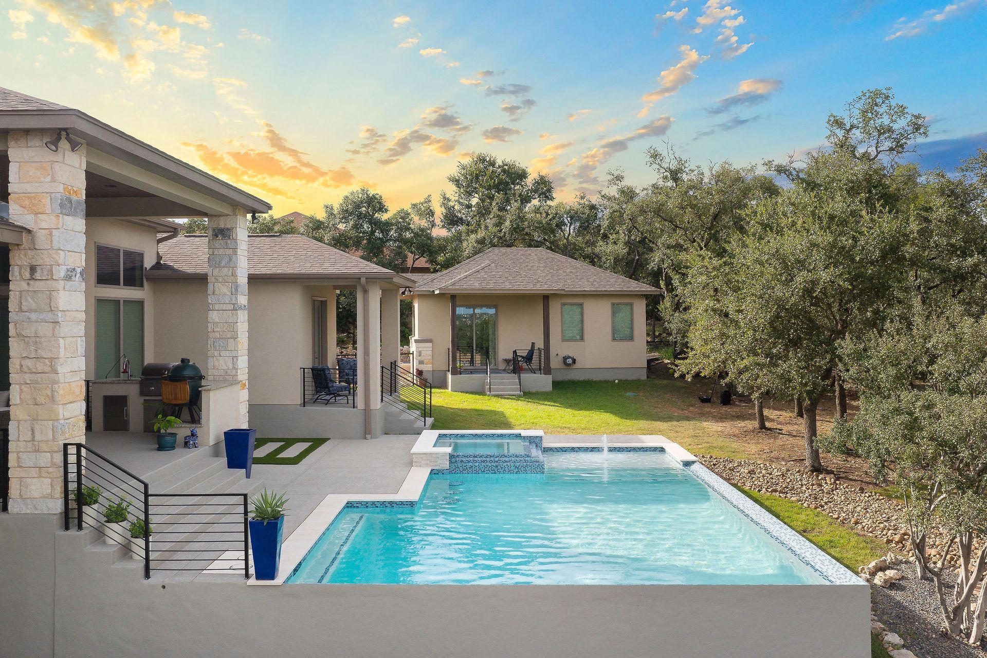 Backyard patio with a swimming pool at sunset, surrounded by a house and trees.