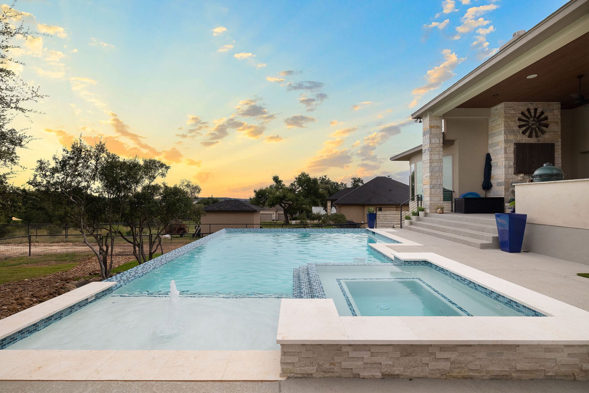Modern backyard pool at sunset beside a house, with patio steps and blue sky.