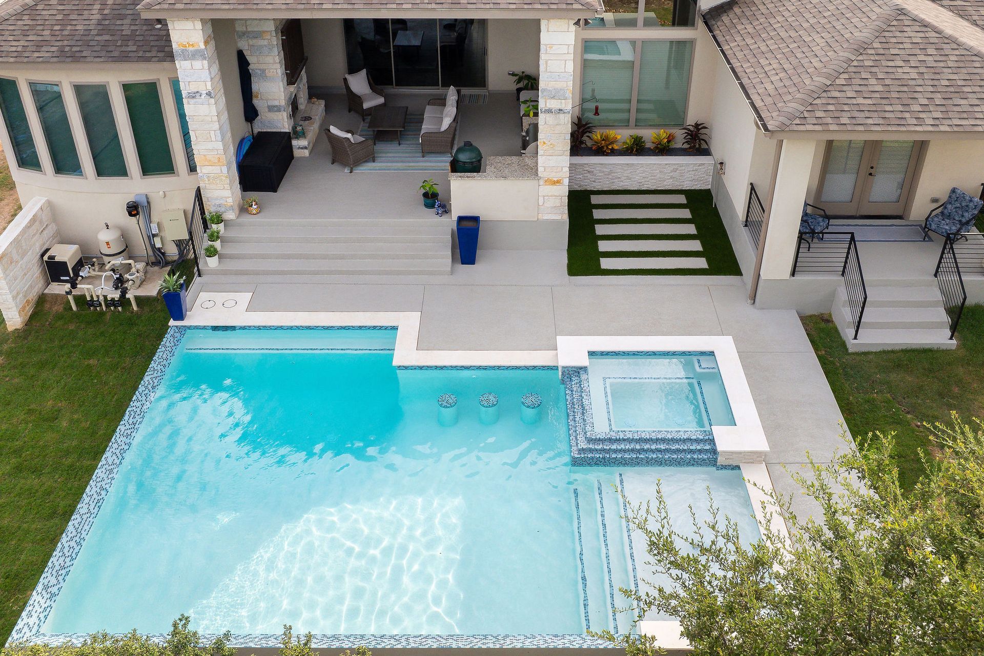 Modern backyard with turquoise pool, hot tub, and patio seating beside a white house