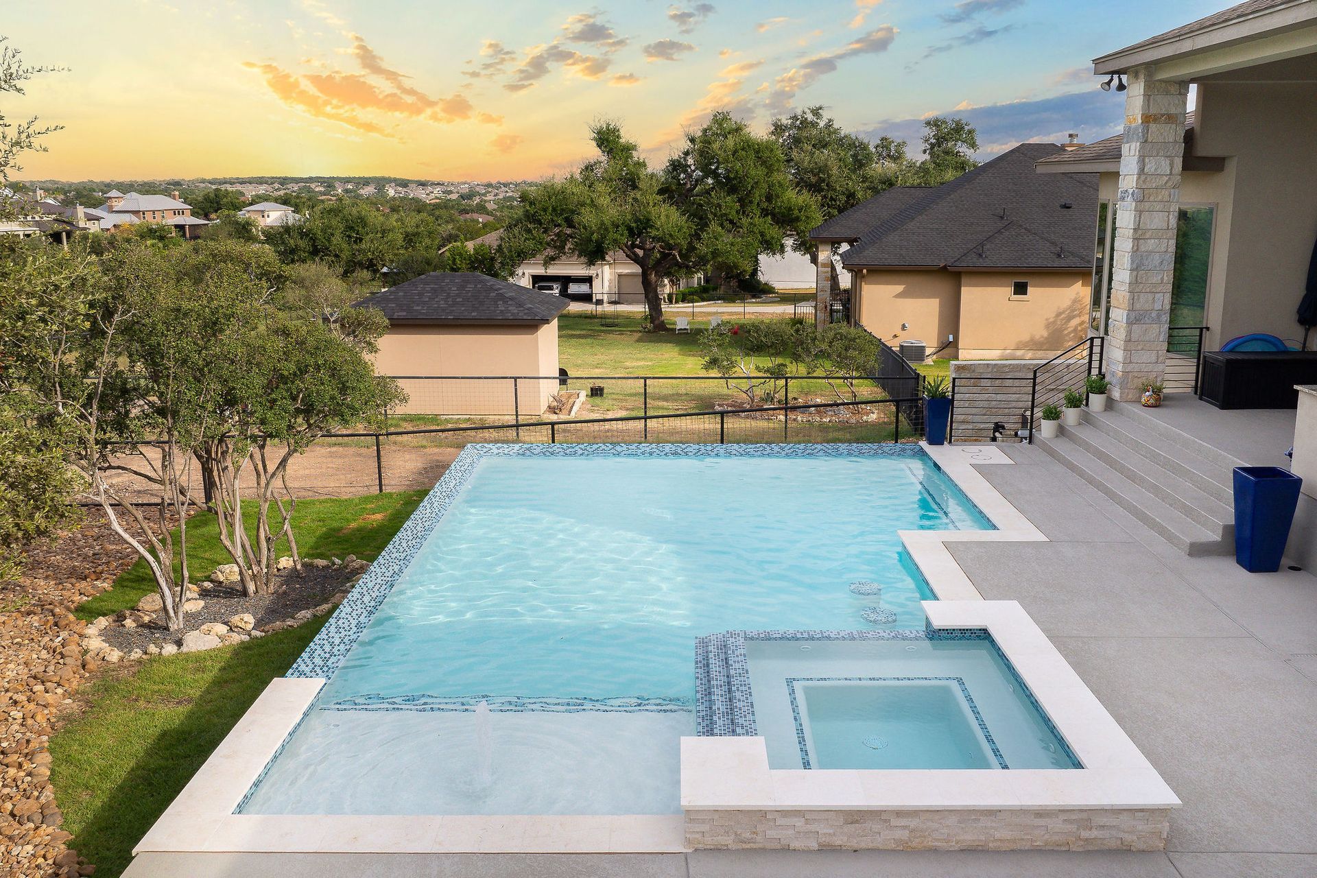 Backyard patio with a turquoise swimming pool and spa at sunset, overlooking neighboring homes