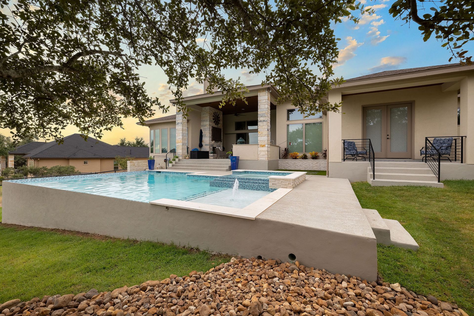Modern backyard with a blue pool, white patio, and covered outdoor seating at sunset