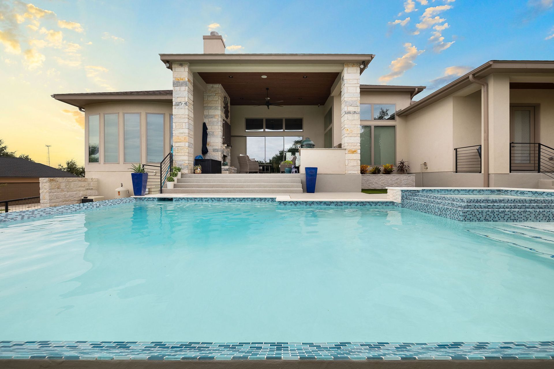 Modern home with a turquoise swimming pool and covered patio at sunset