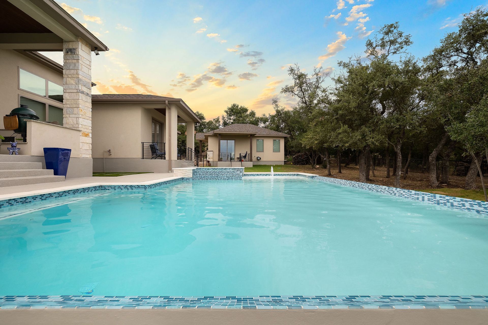 Backyard swimming pool beside a house at sunset, with trees and a blue sky