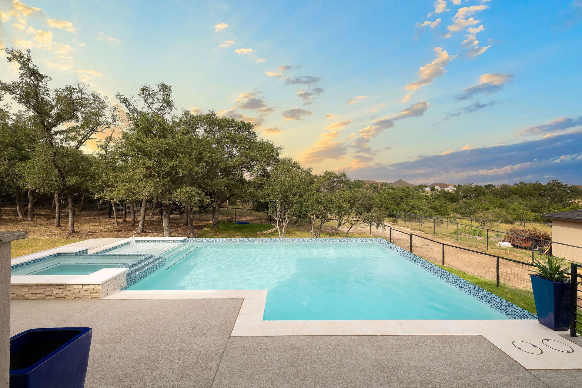 Outdoor pool with turquoise water, white deck, trees, and a sunset sky over the horizon