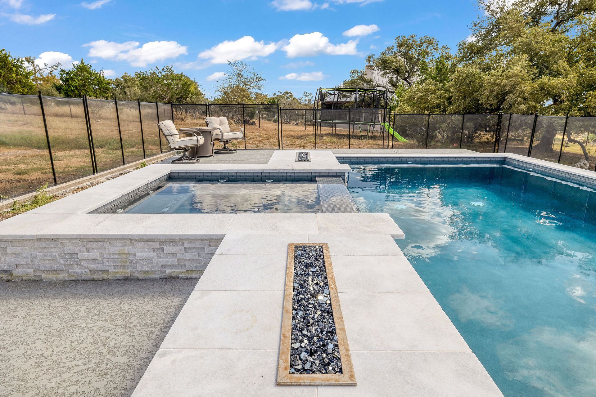 Modern backyard pool with built-in spa, stone coping, and desert landscaping under a clear sky