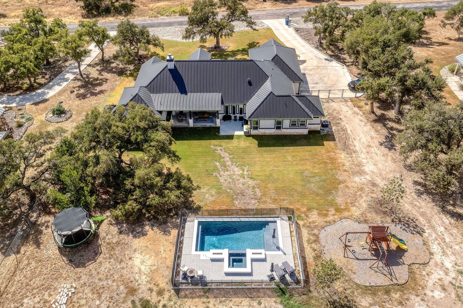 Aerial view of a white house with a dark roof, pool, and trees on a large property.