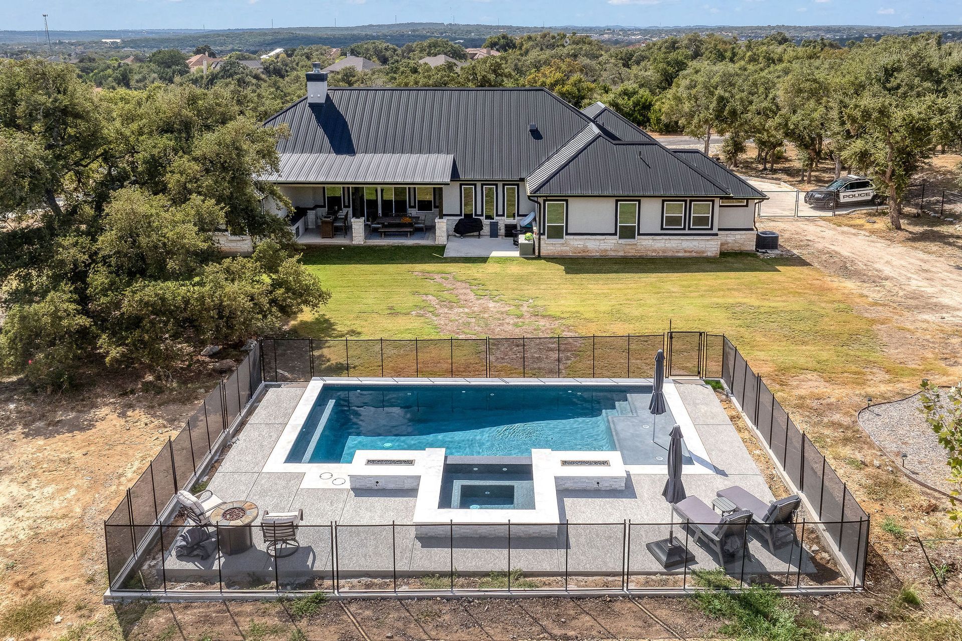 Aerial view of a modern house with a fenced backyard pool and surrounding dry landscape.
