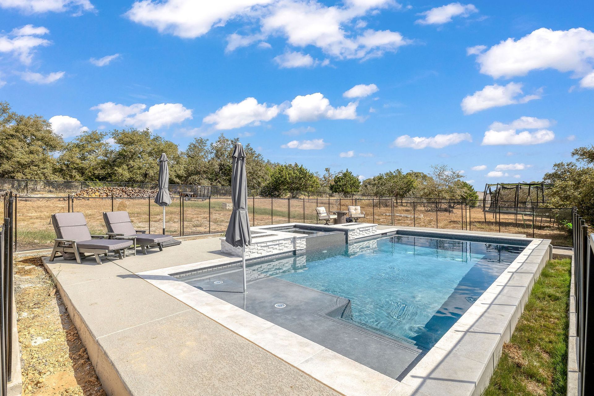 Backyard pool with lounge chairs, umbrella, and clear blue water under a sunny sky