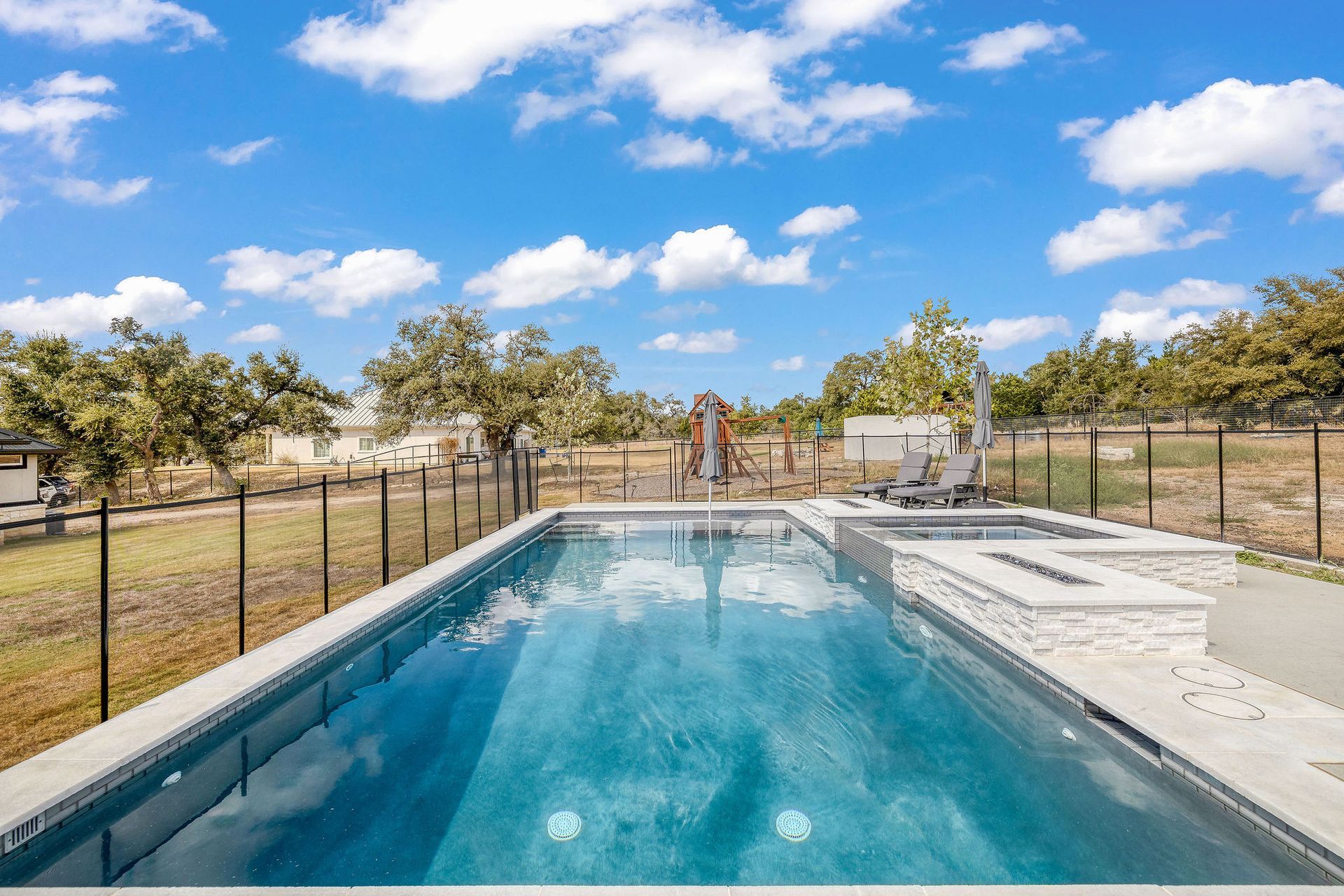 Rectangular outdoor swimming pool beside a fenced yard under a bright blue sky