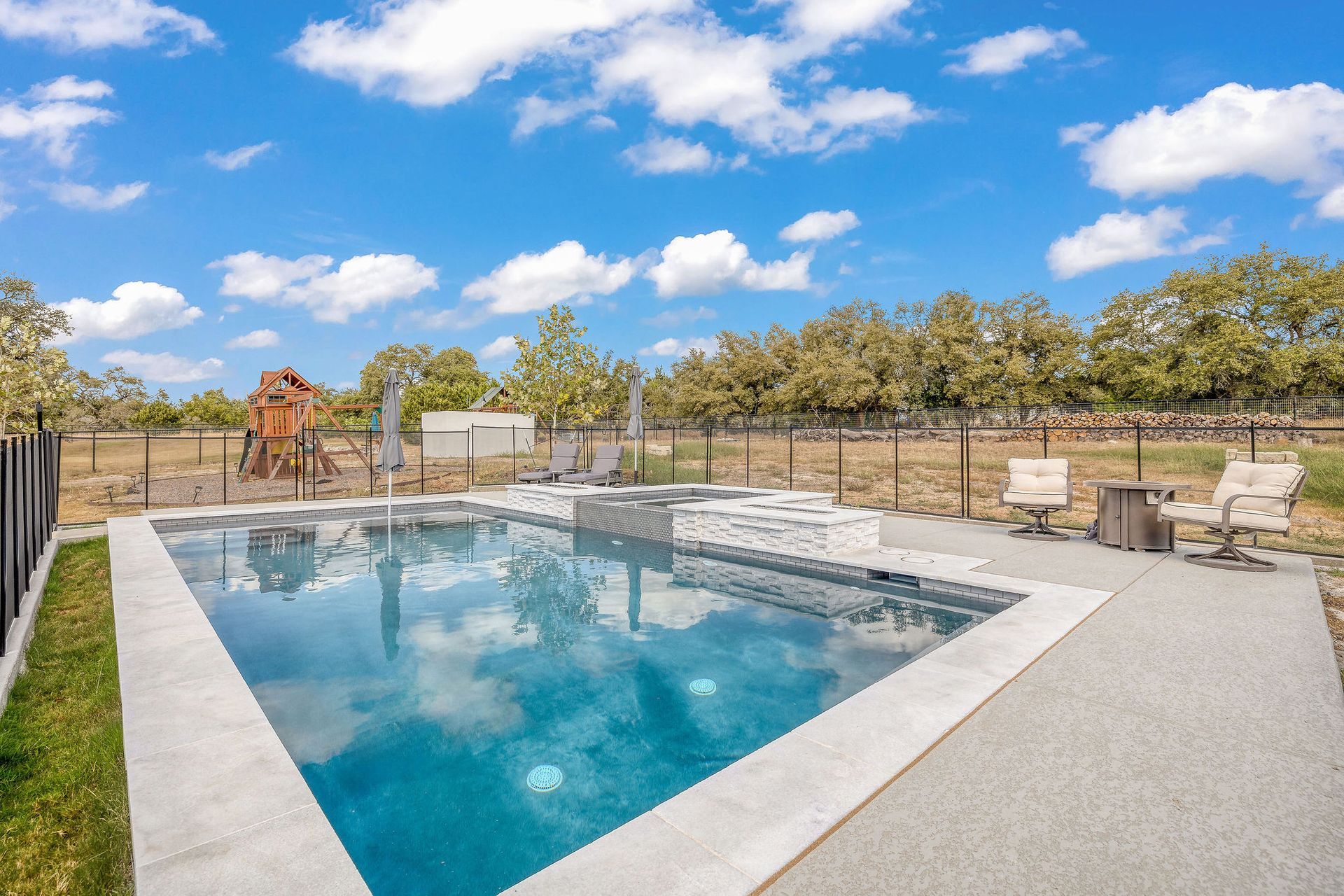 Backyard swimming pool with lounge chairs, patio, and blue sky with clouds