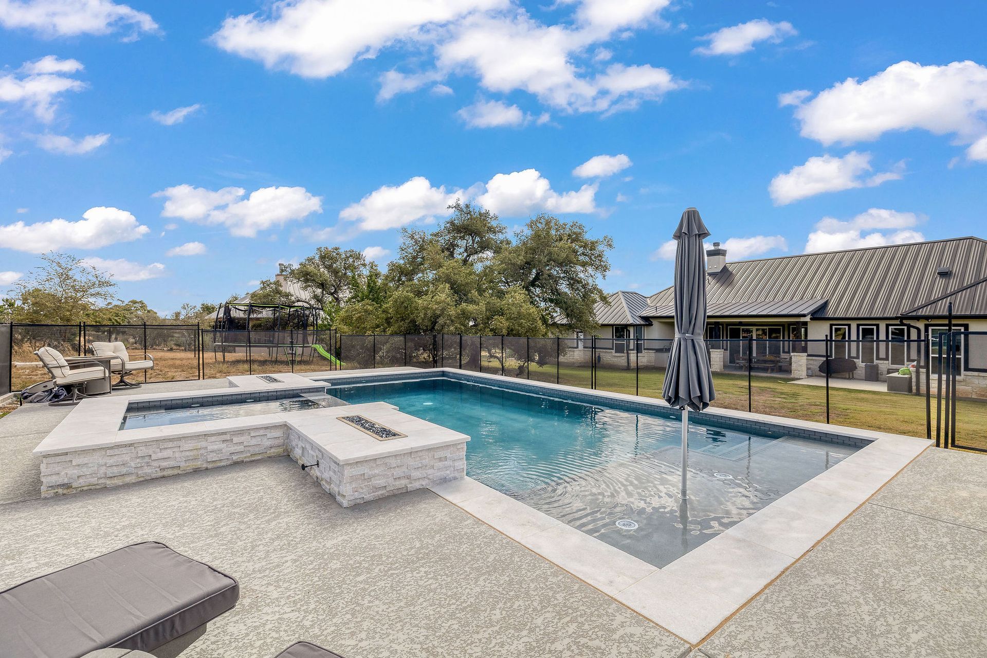 Backyard pool with built-in spa, umbrella, and patio under a blue sky