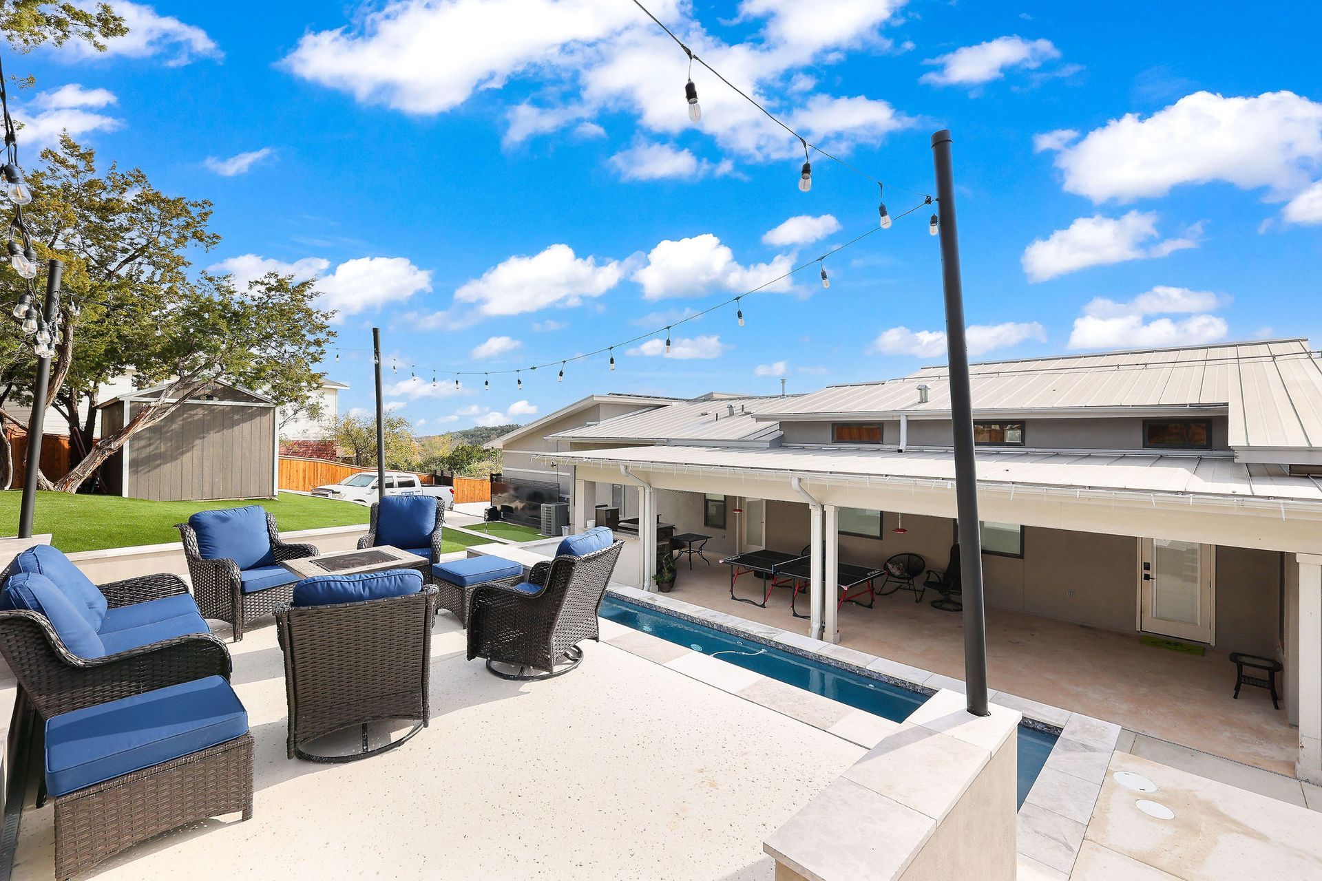 Sunny patio with blue wicker chairs beside a swimming pool and covered outdoor seating area.