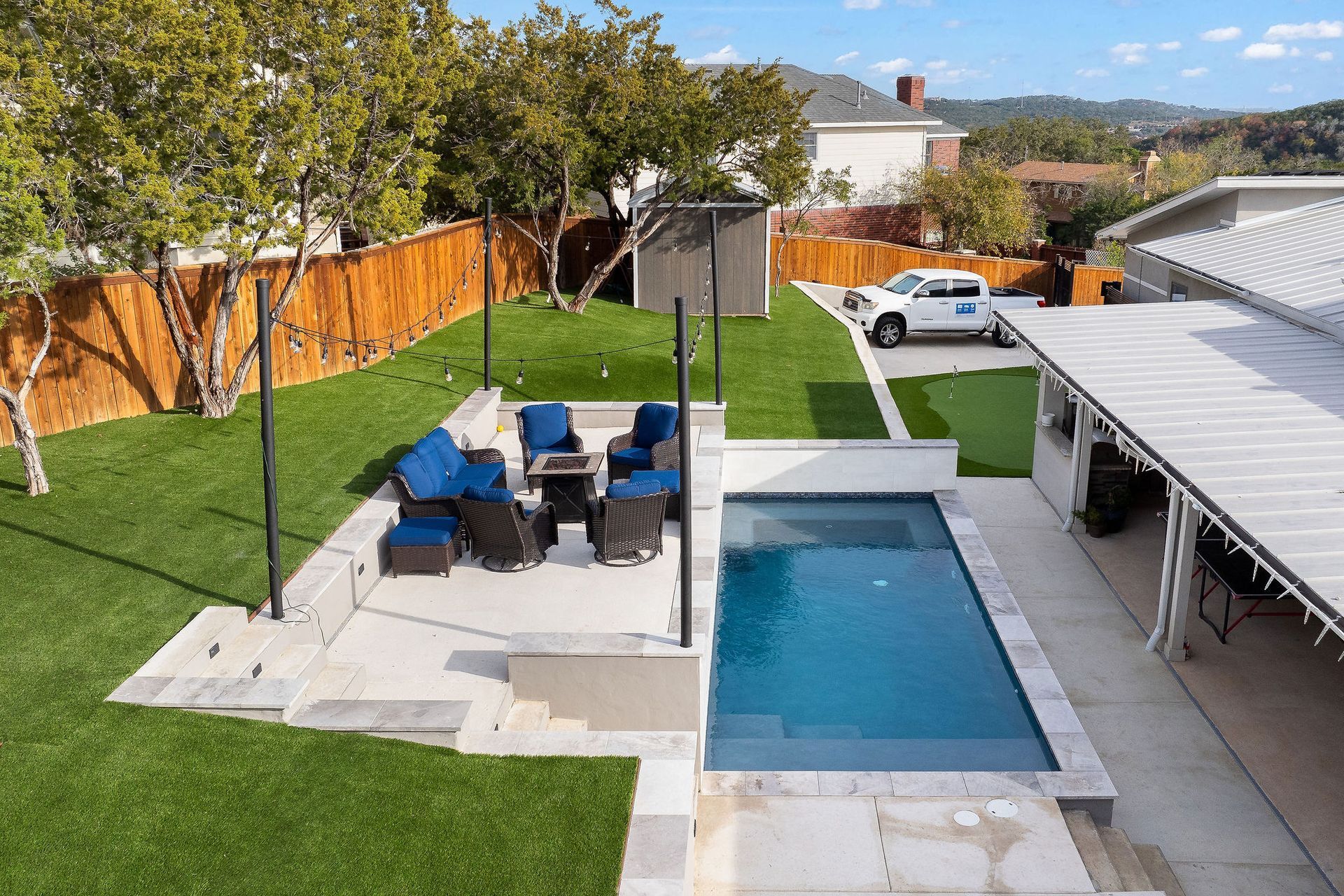 Backyard with swimming pool, patio dining set, green lawn, and a white car by the driveway.