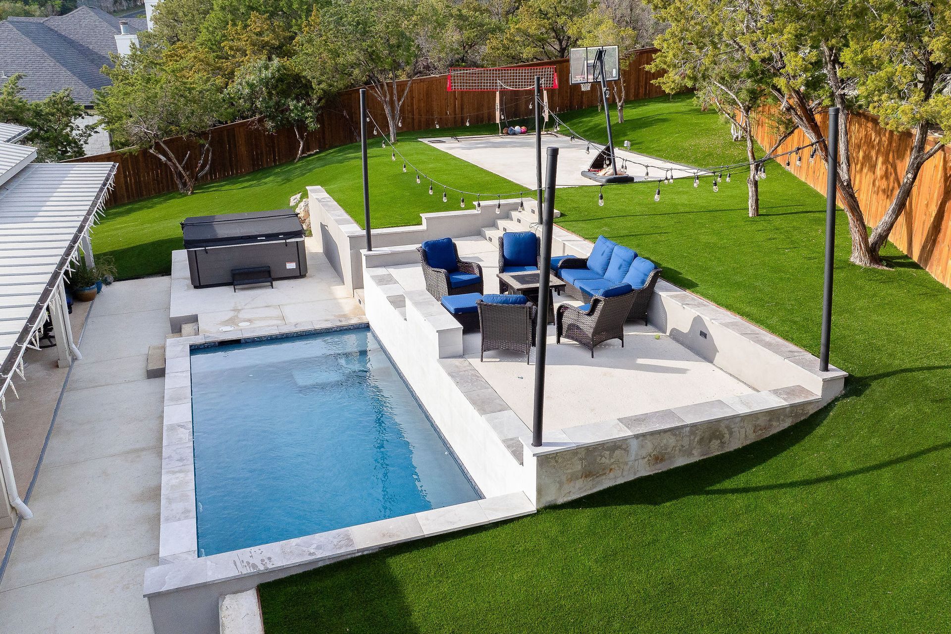 Modern backyard with a swimming pool, outdoor lounge seating, and a covered patio on green lawn.