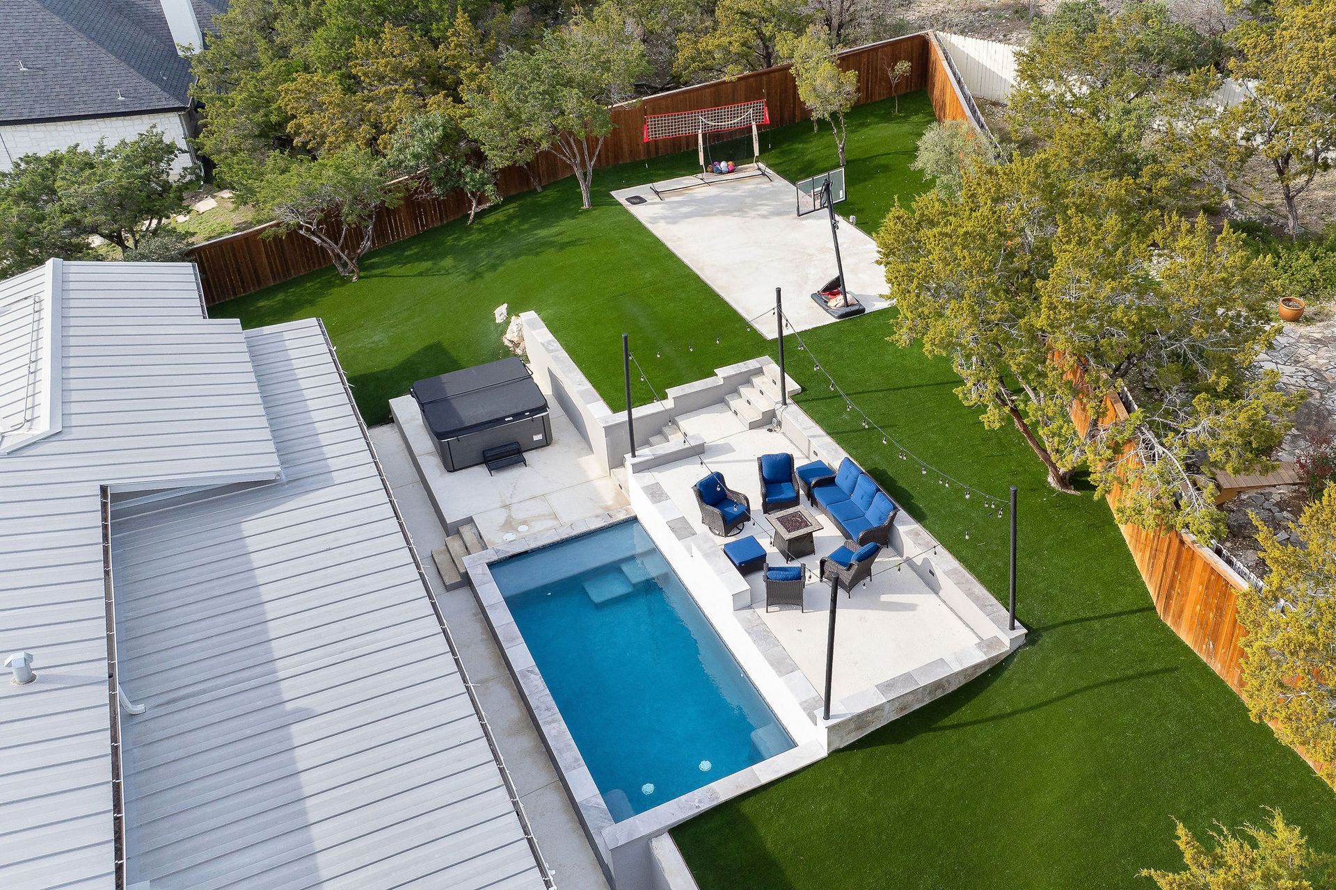 Backyard with a blue pool, white patio, lounge chairs, and outdoor dining beside a grassy lawn