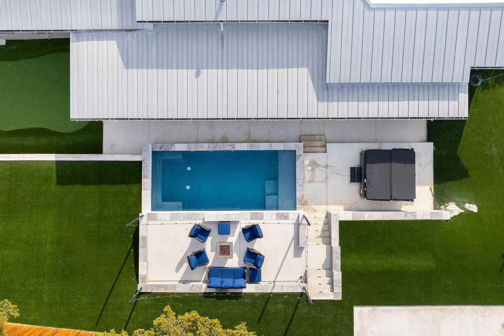 Aerial view of a backyard pool, patio seating, and a house with a white roof and green lawn.