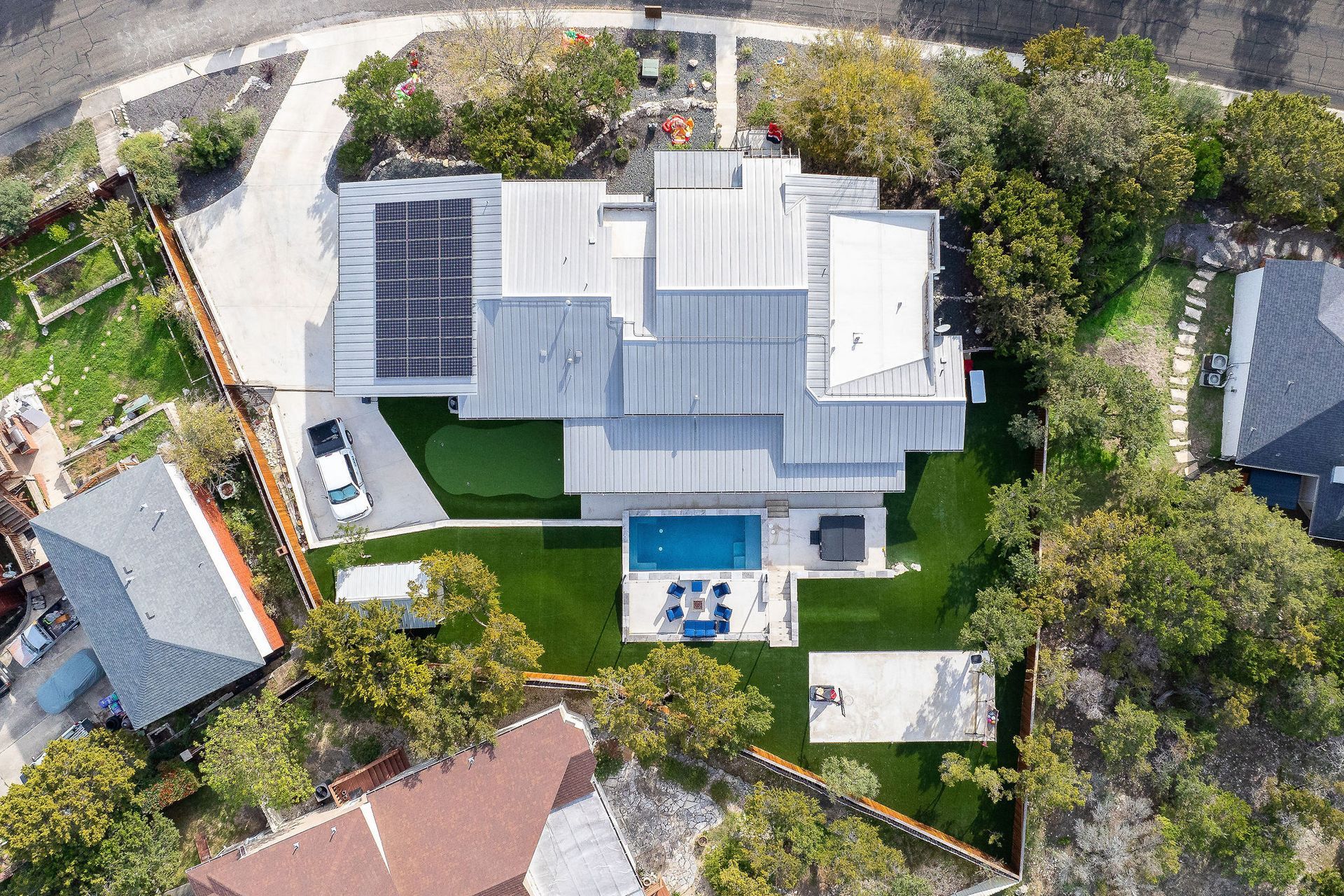 Aerial view of a modern white house with a backyard pool, patio, and surrounding trees
