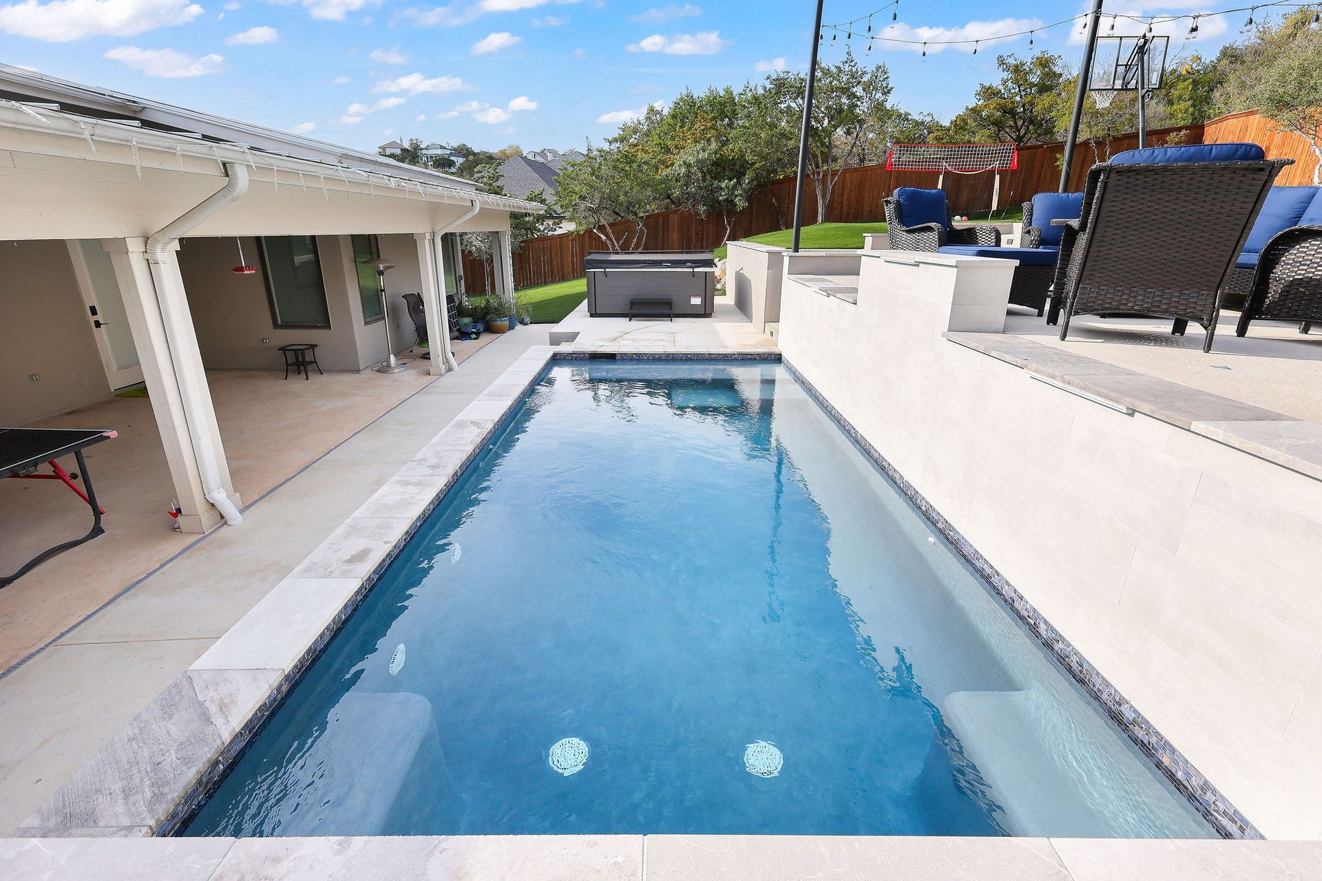 Backyard swimming pool beside a patio, with lounge chairs and clear blue water under a sunny sky