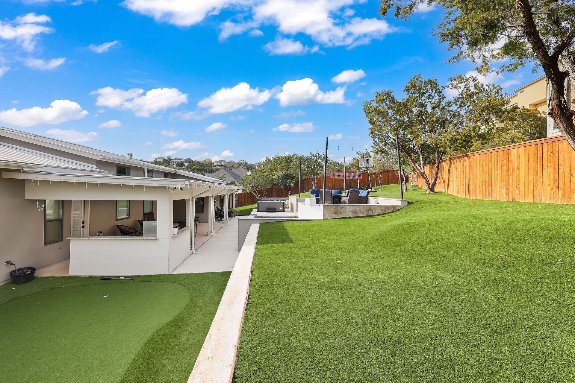 Backyard with green lawn, patio, pool, and white house under a blue sky