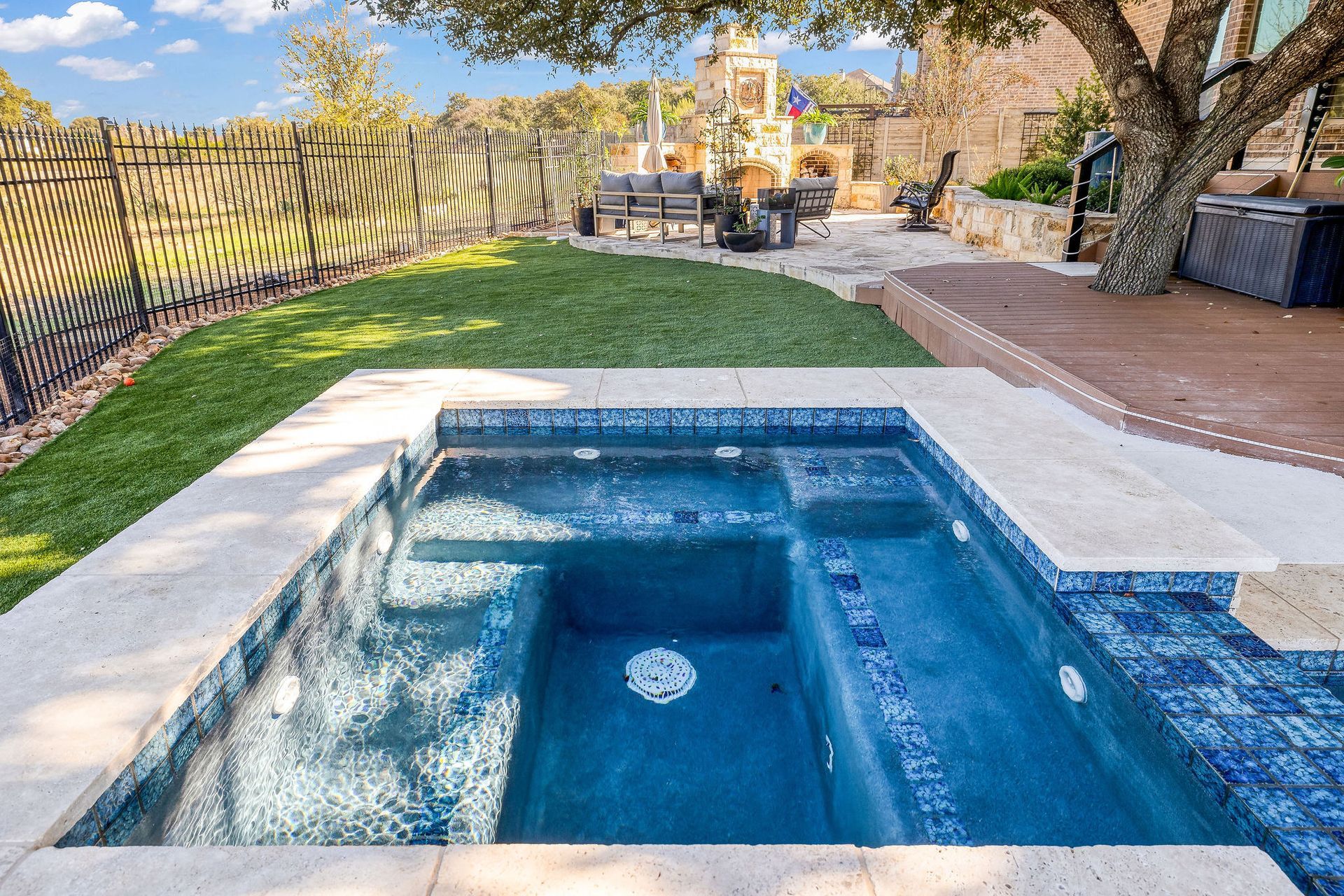 Backyard with a blue hot tub beside a pool, lawn, and patio under a sunny sky