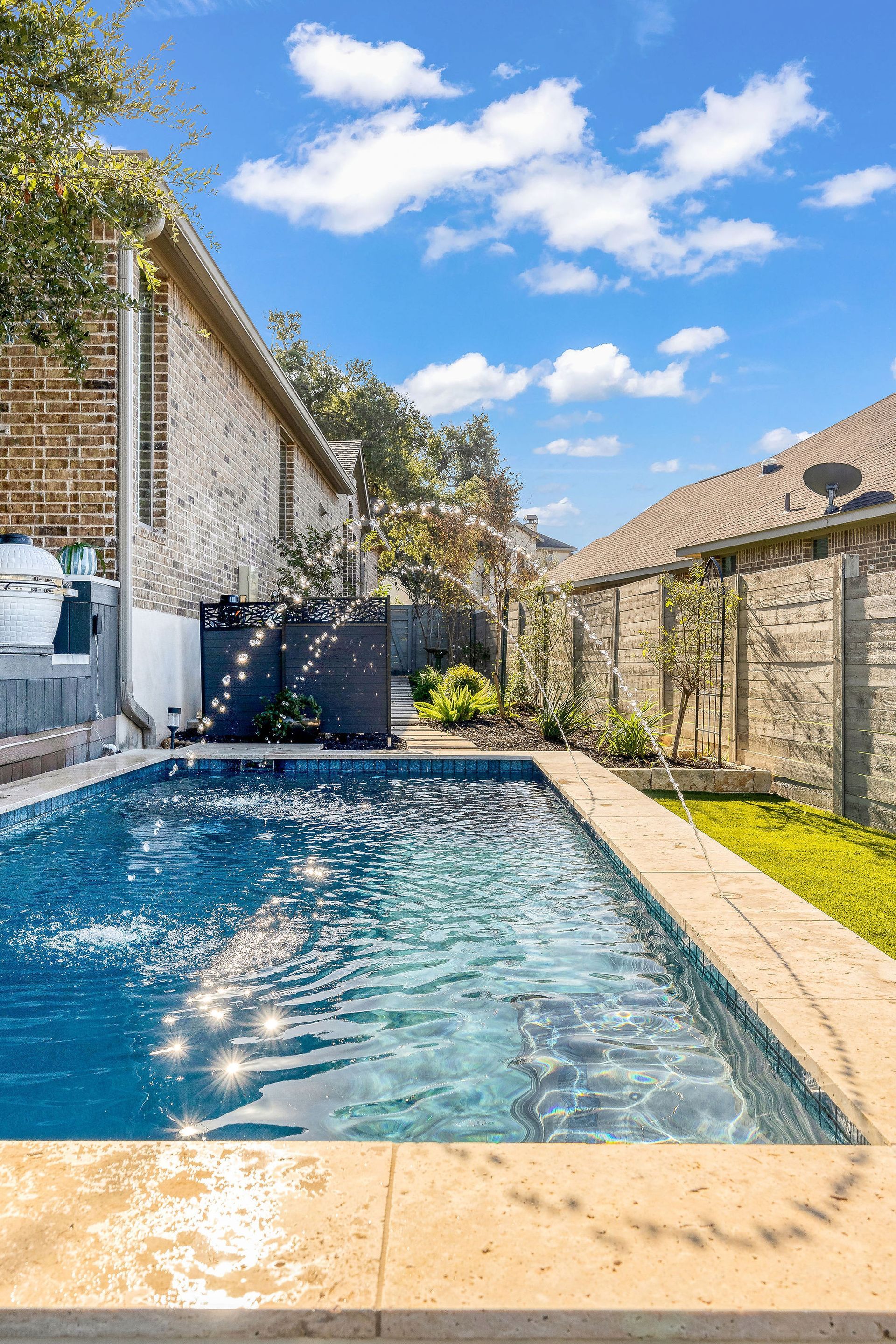 Rectangular blue swimming pool in a stone-walled courtyard under a bright blue sky
