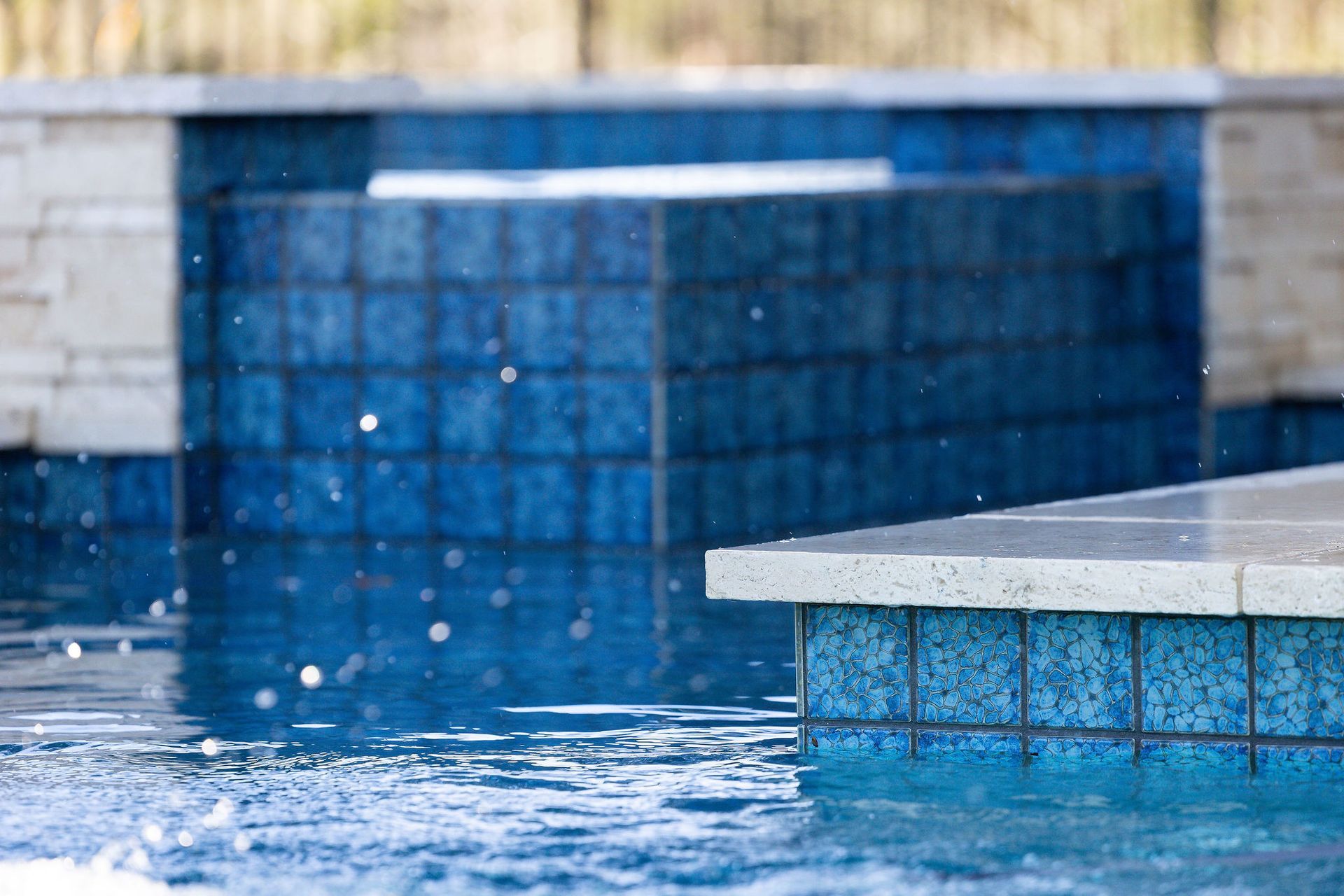 Blue tiled swimming pool water with a raised edge and water splashing near the surface