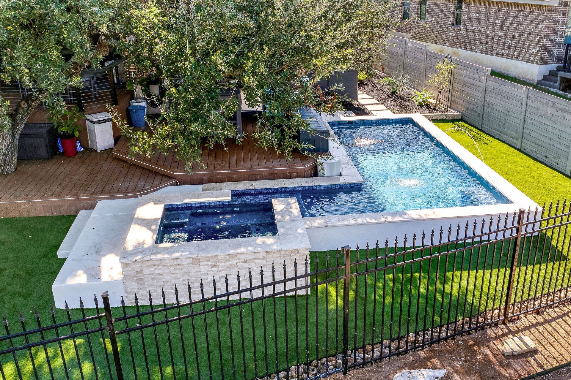 Backyard with a rectangular swimming pool, hot tub, patio, and lawn behind a black fence