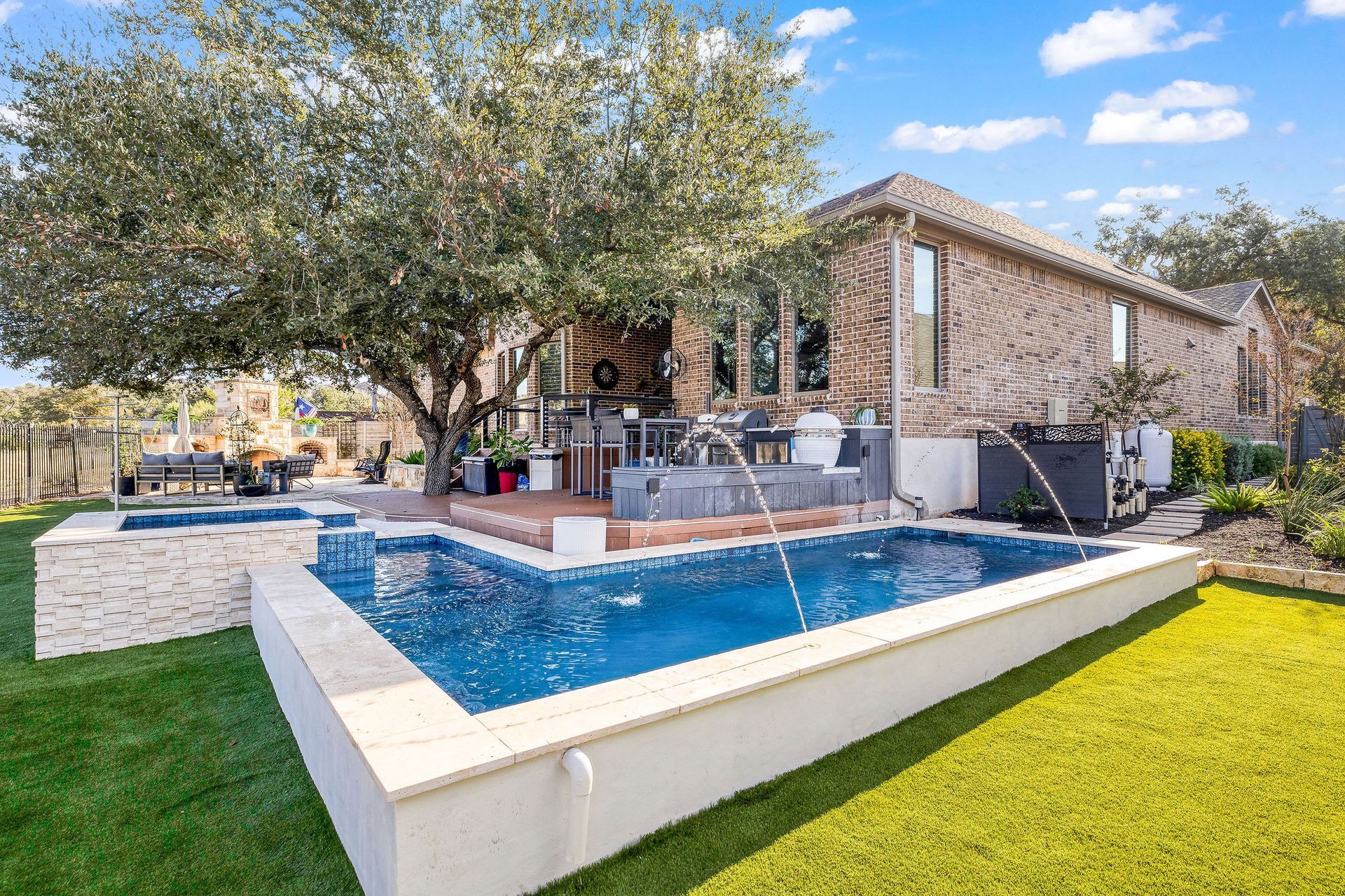 Backyard with a blue swimming pool, patio seating, and a stone house under a large tree