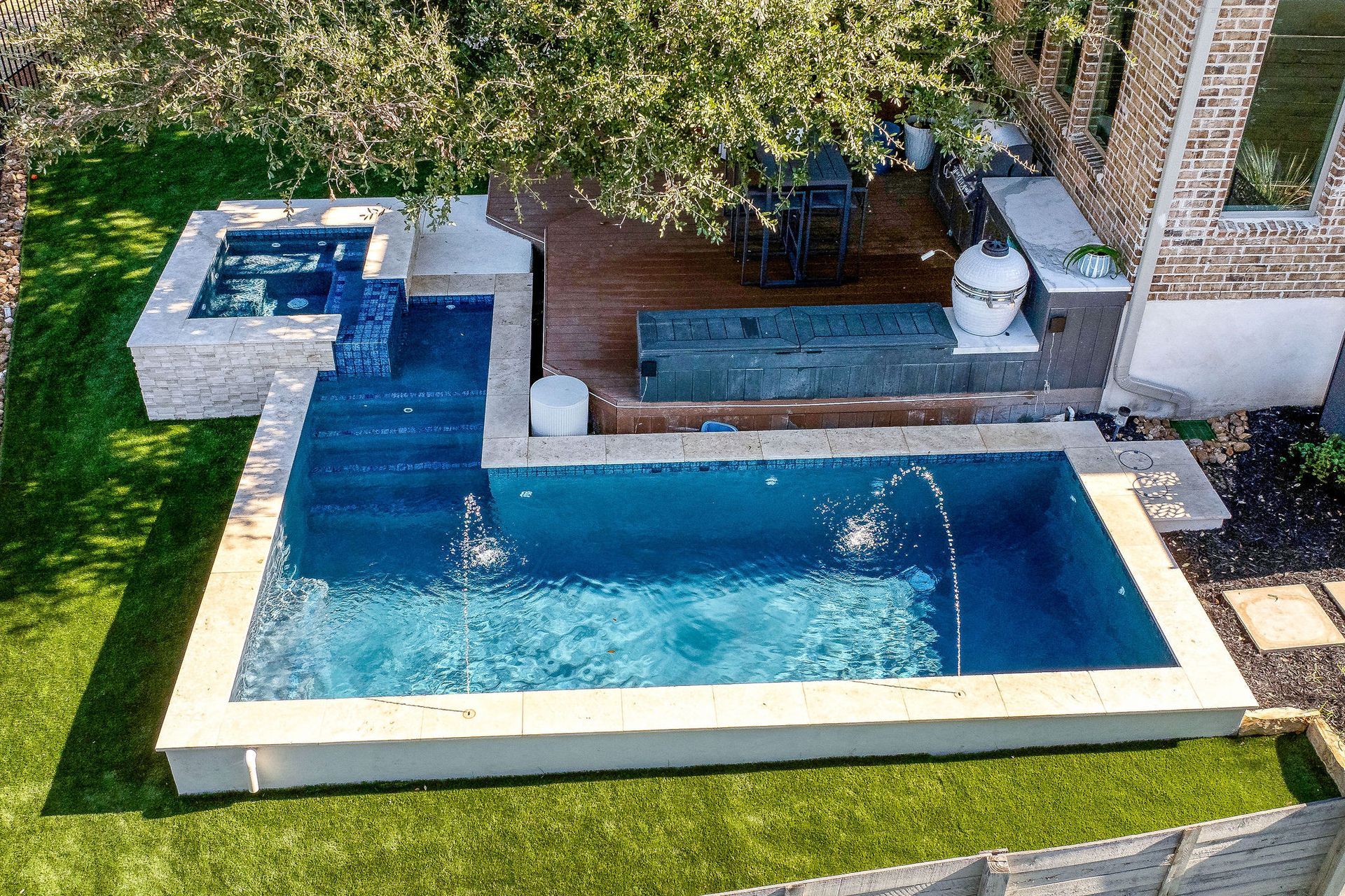 Modern backyard pool with a blue water feature and hot tub beside a patio and lawn