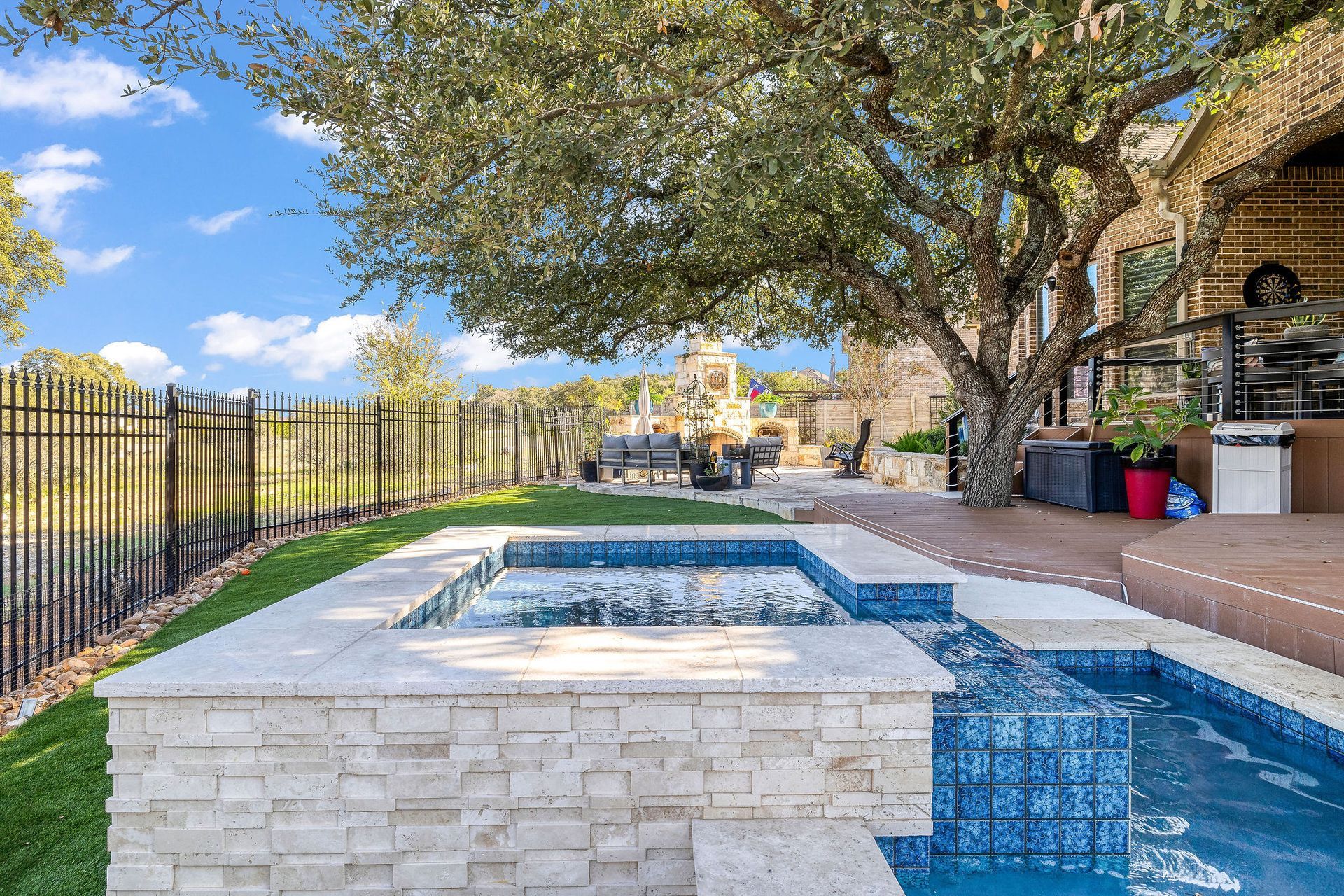 Backyard pool with stone spa, blue-tiled water, trees, and a patio beside a house