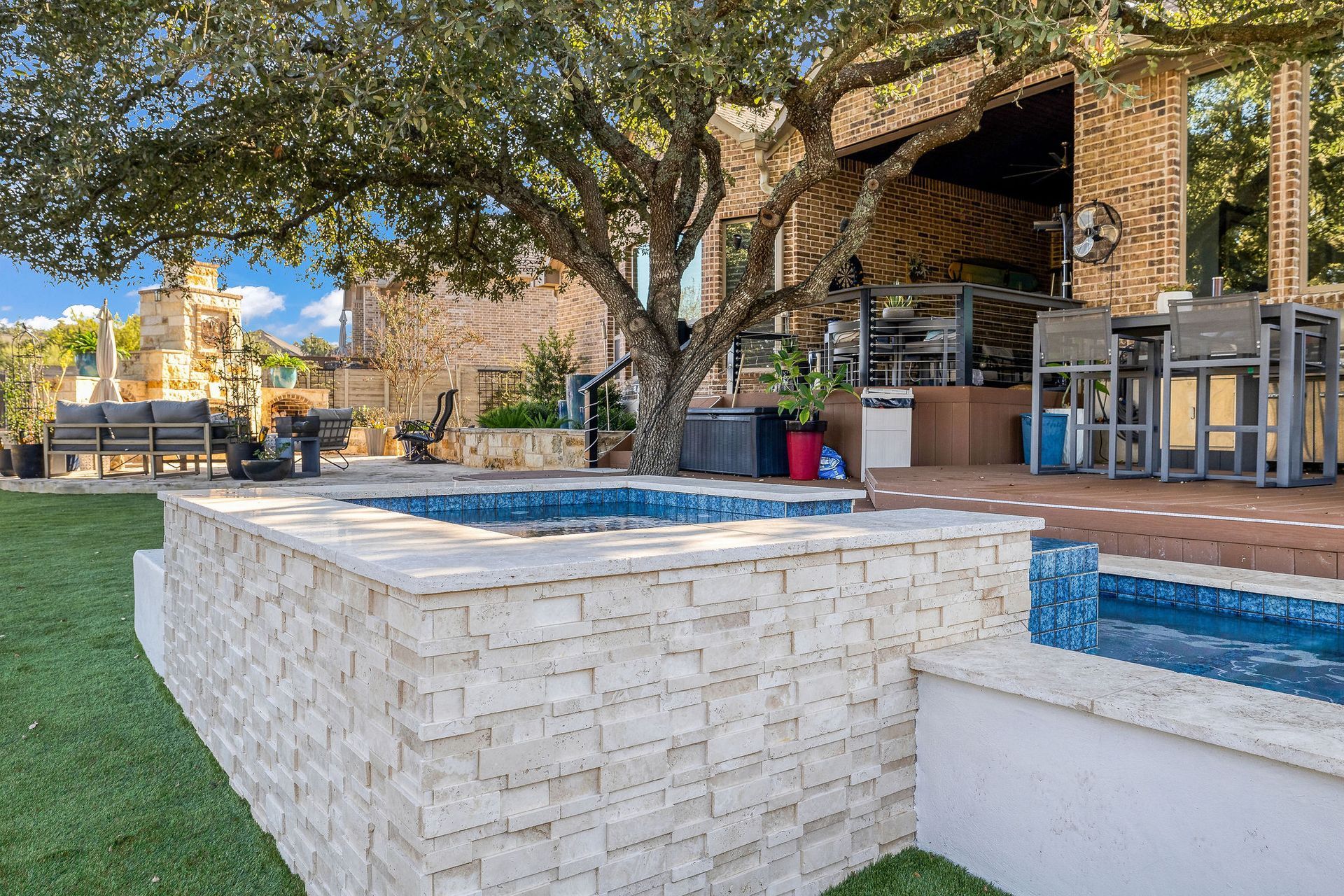 Modern backyard patio with a stone hot tub, pool edge, trees, and a covered outdoor bar area