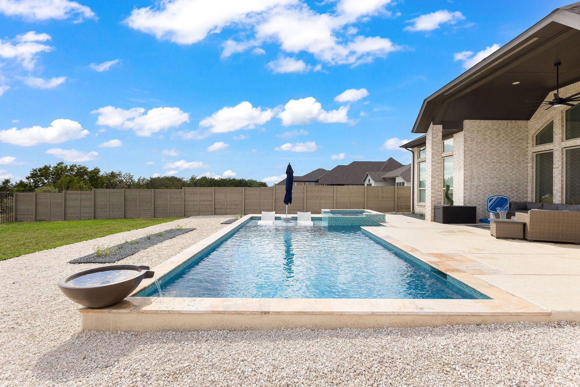 Backyard patio with a rectangular swimming pool, lounge chairs, and a covered outdoor seating area under a blue sky