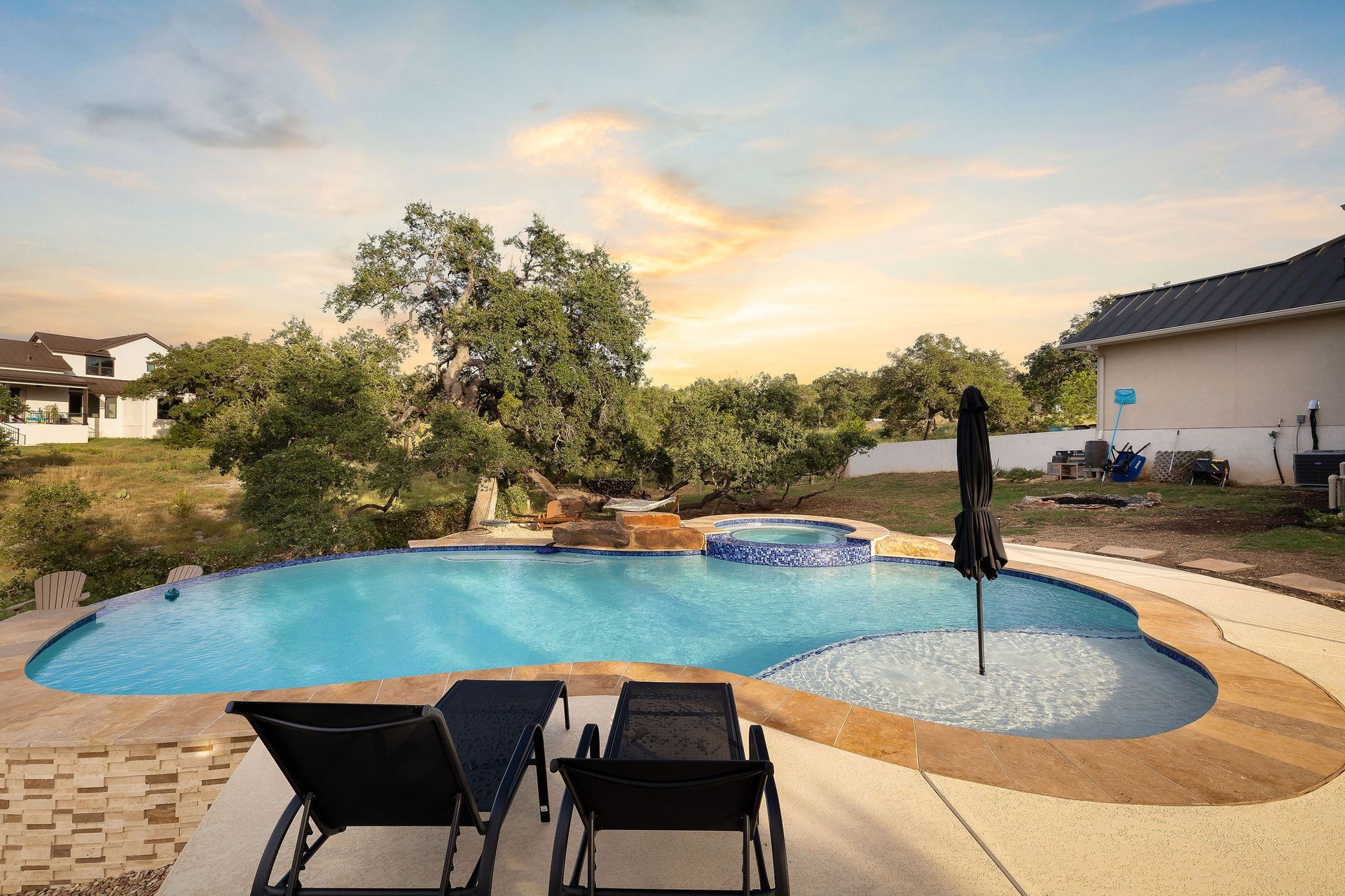 Backyard pool with patio chairs, umbrella, and sunset sky