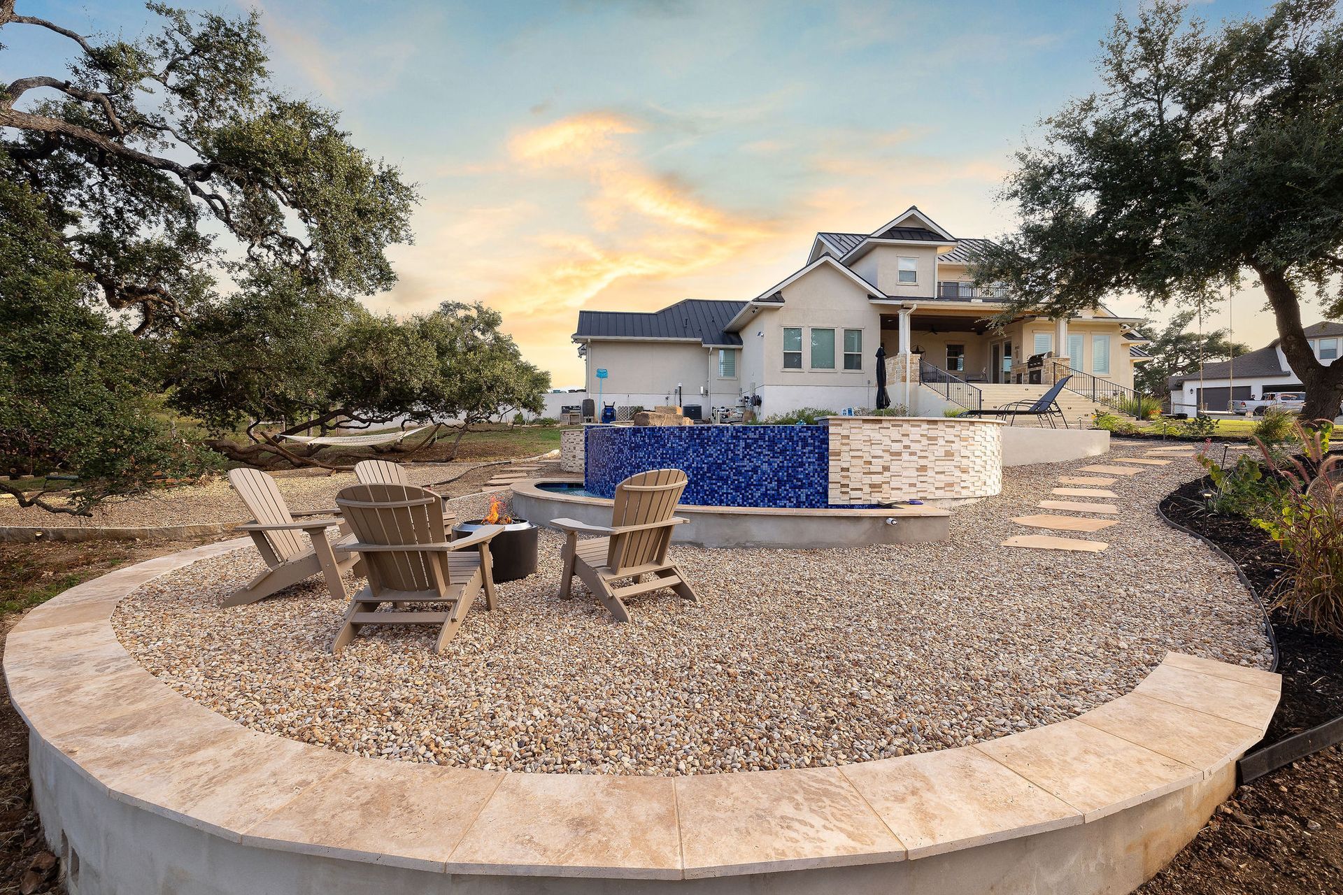 Patio with fire pit, outdoor seating, and a blue tiled pool beside a modern house at sunset