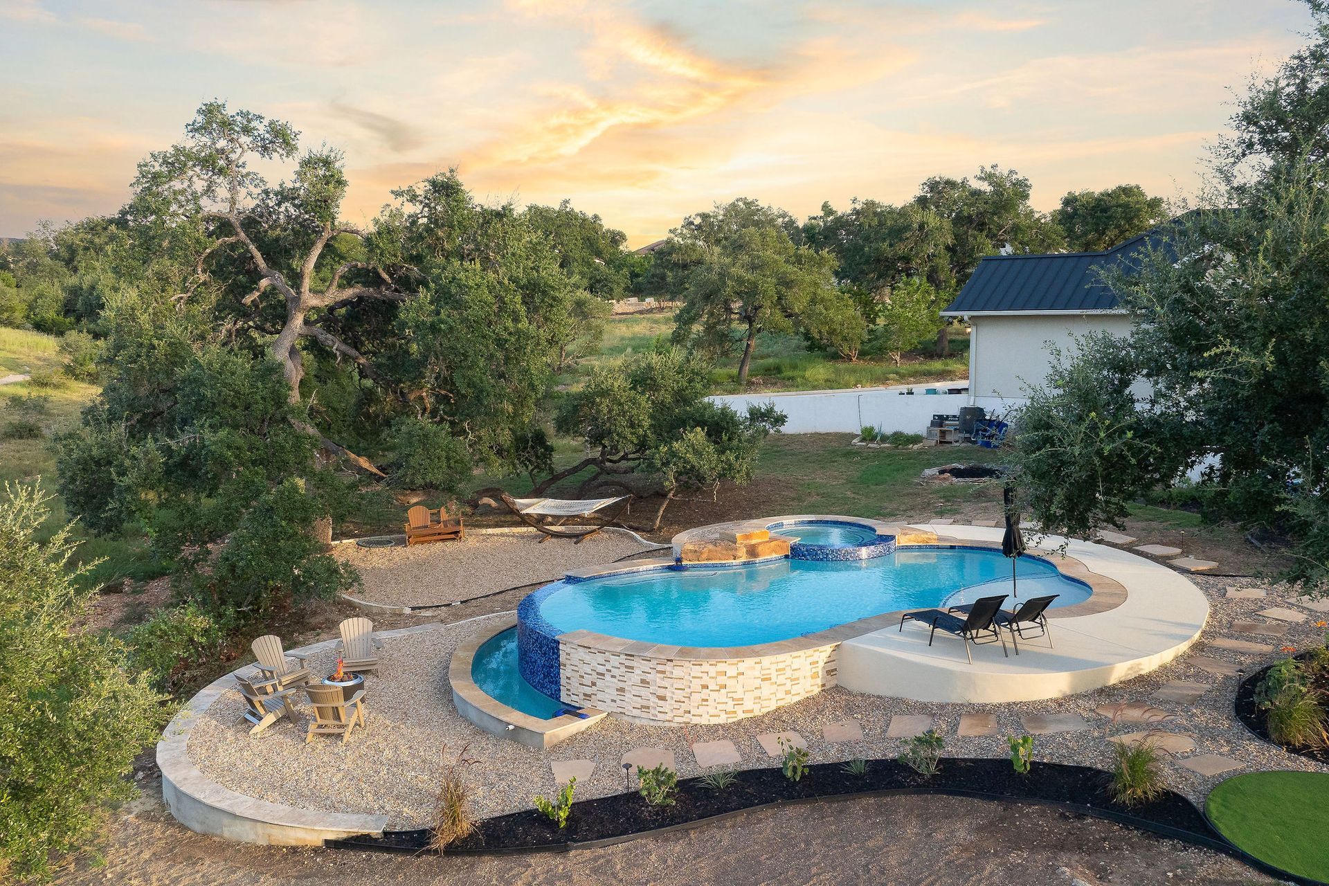 Top-down view of a curvy backyard pool with stone paving, a small spa, and surrounding greenery