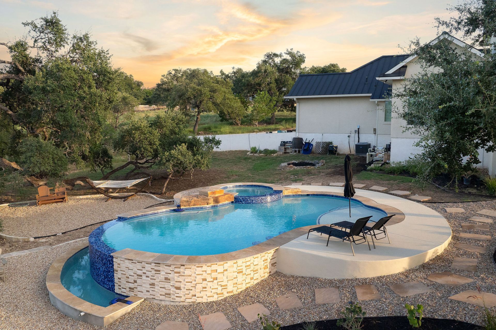 Top-down view of a curvy backyard pool with stone paving, a small spa, and surrounding greenery