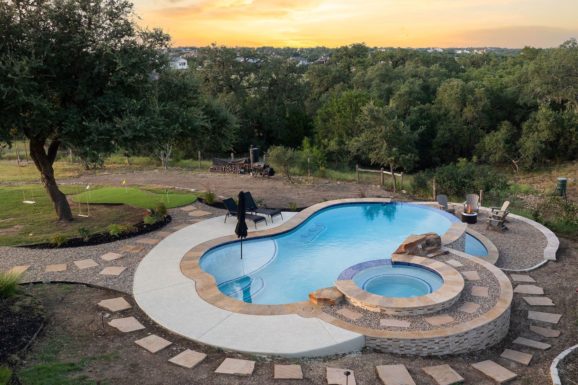 Top-down view of a curvy backyard pool with stone paving, a small spa, and surrounding greenery