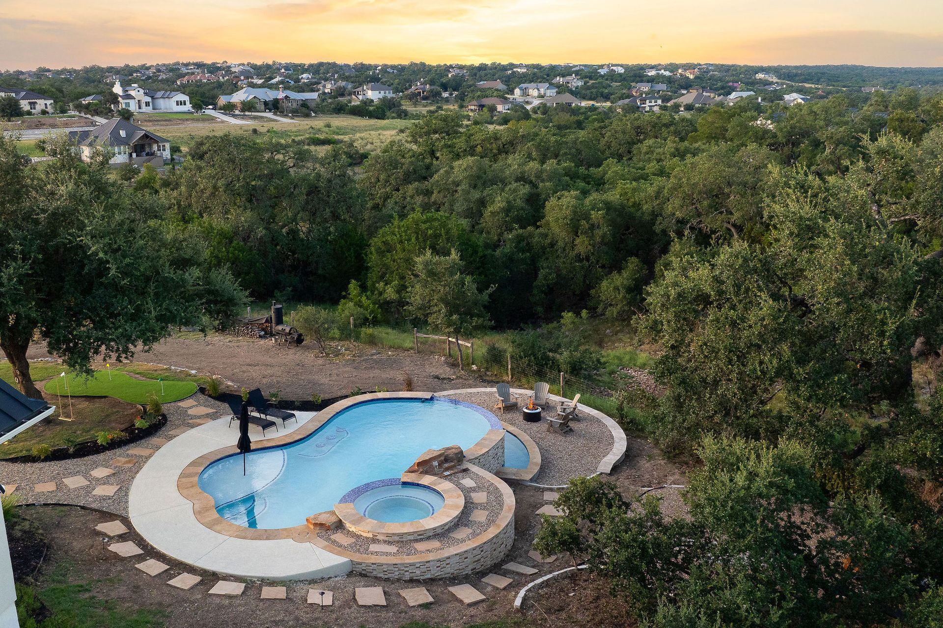 Top-down view of a curvy backyard pool with stone paving, a small spa, and surrounding greenery