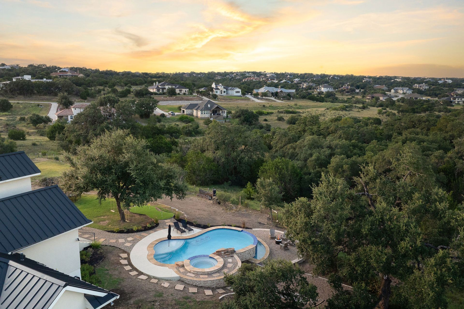 Top-down view of a curvy backyard pool with stone paving, a small spa, and surrounding greenery