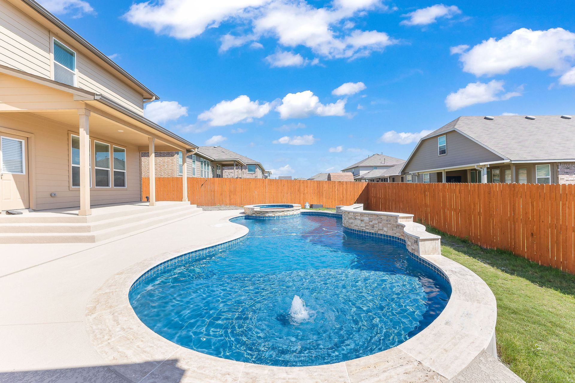 Modern backyard with a turquoise pool, lounge chairs, trees, and a sunset sky over hills.