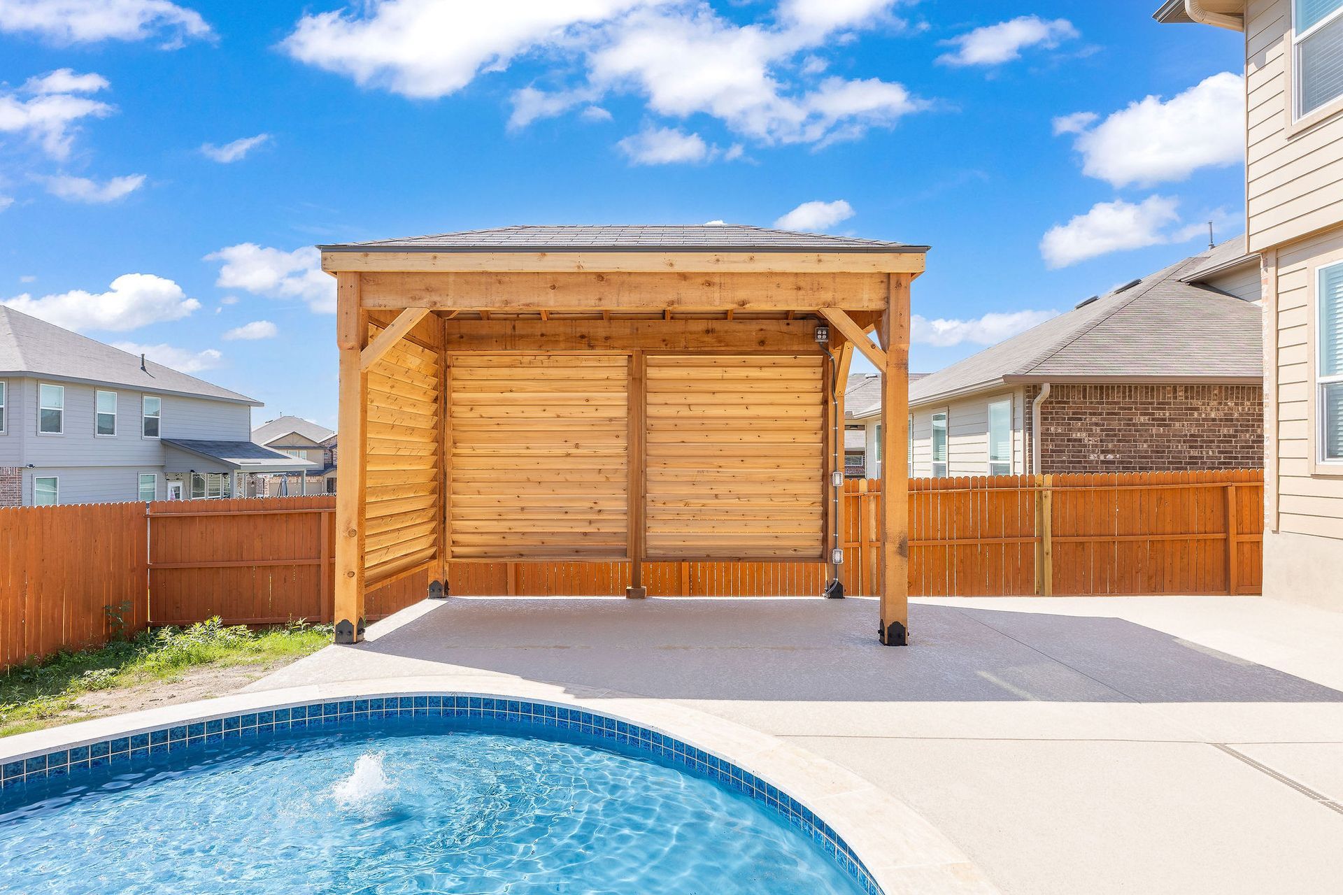 Modern backyard with a turquoise pool, lounge chairs, trees, and a sunset sky over hills.
