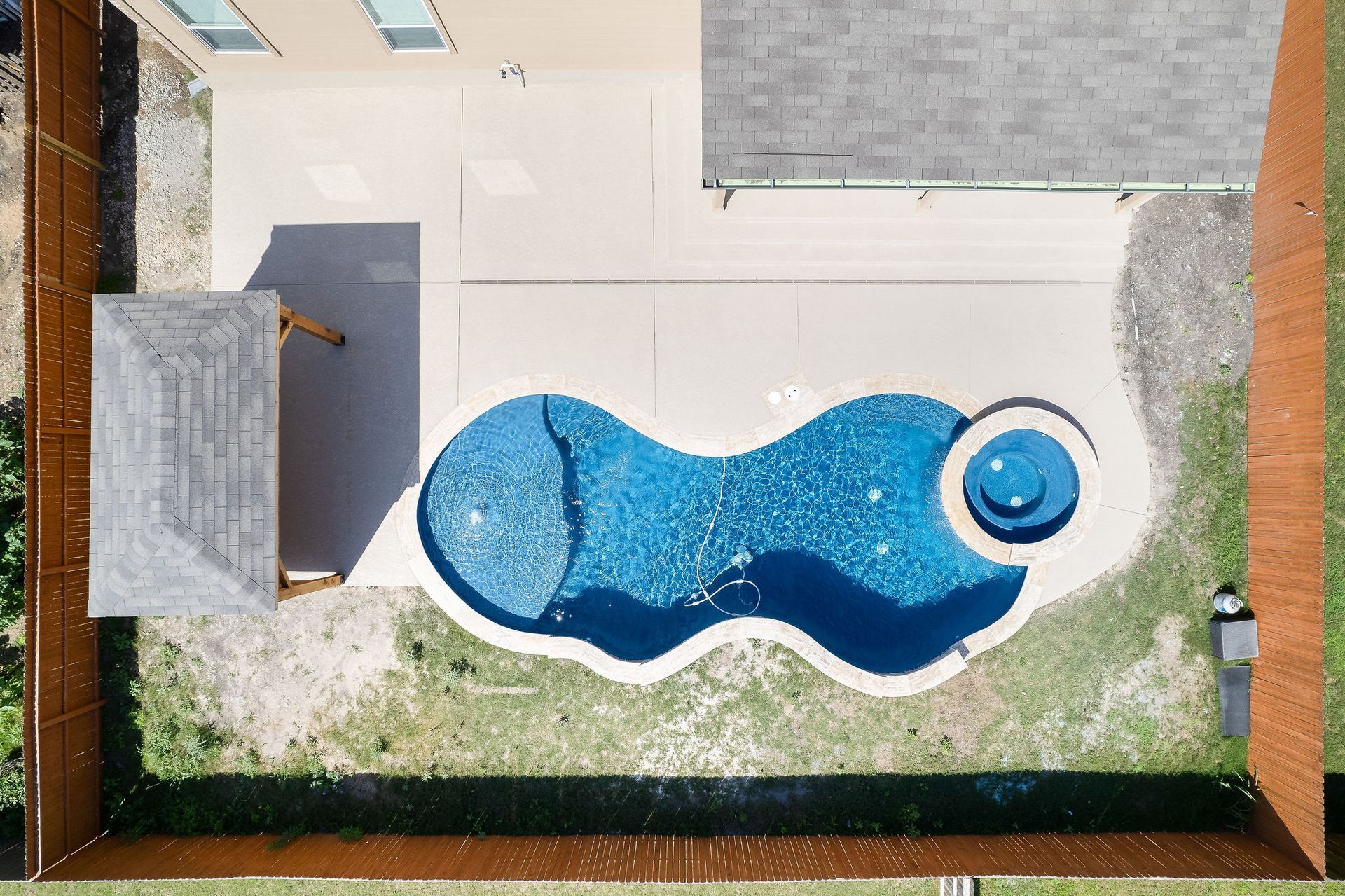 Modern backyard with a turquoise pool, lounge chairs, trees, and a sunset sky over hills.