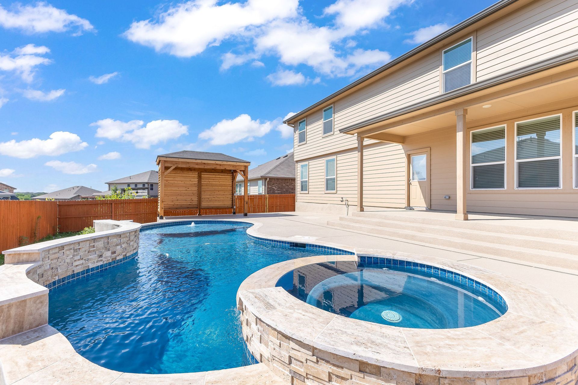 Modern backyard with a turquoise pool, lounge chairs, trees, and a sunset sky over hills.