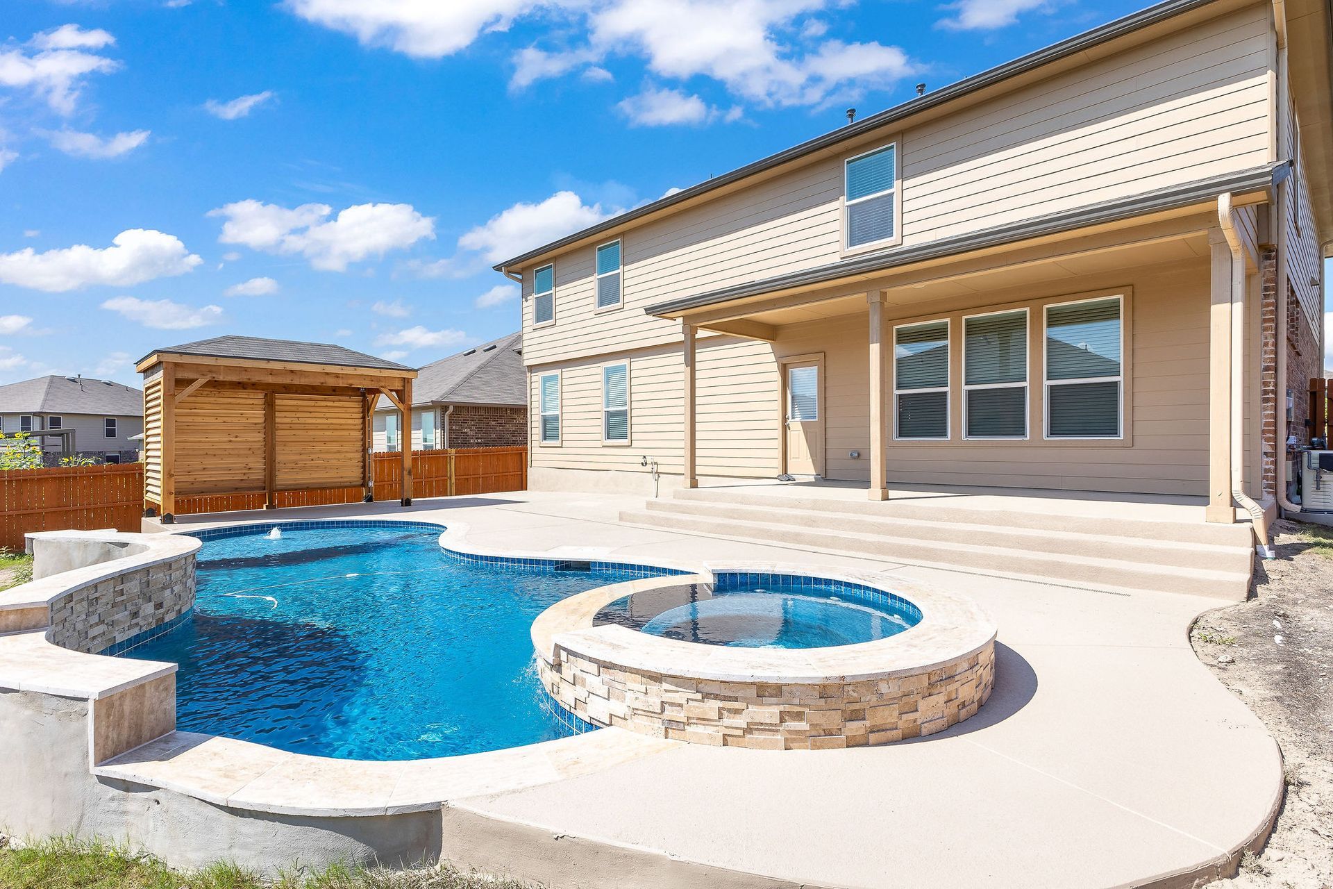 Modern backyard with a turquoise pool, lounge chairs, trees, and a sunset sky over hills.