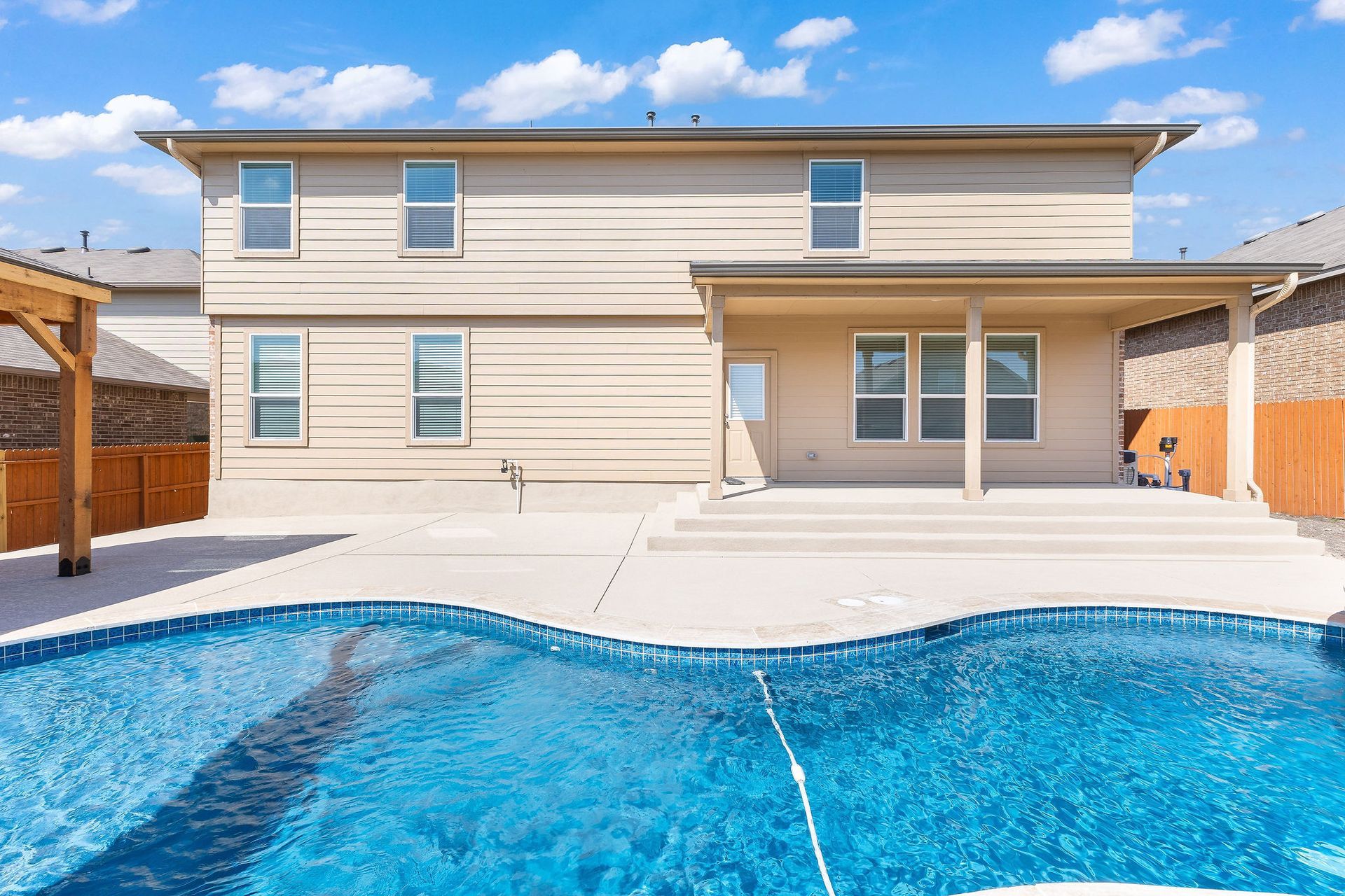 Modern backyard with a turquoise pool, lounge chairs, trees, and a sunset sky over hills.